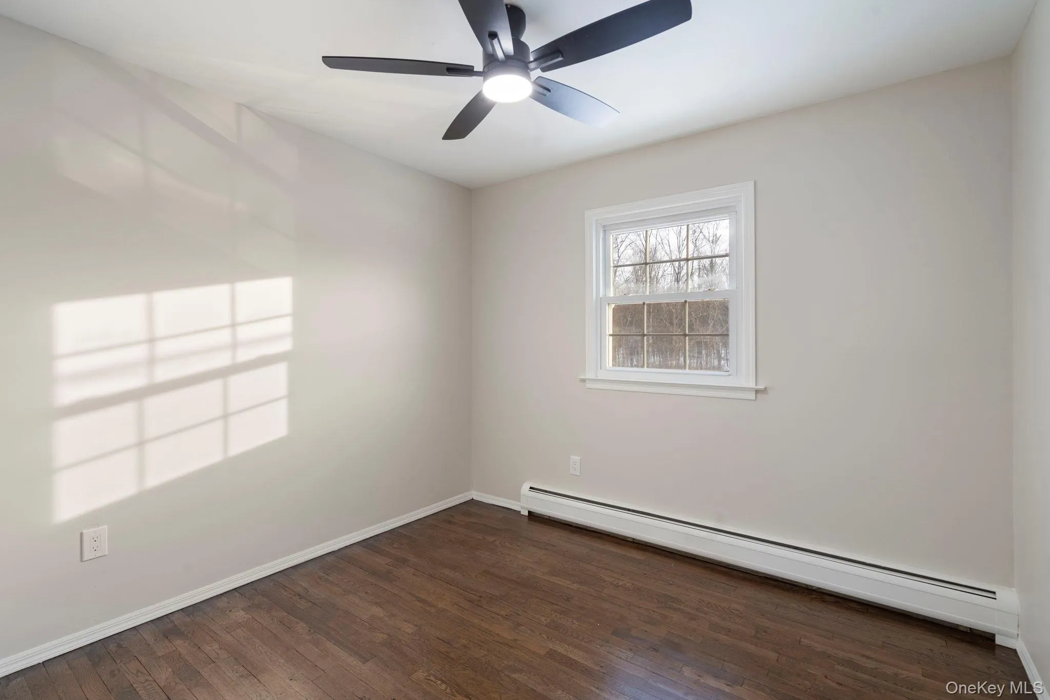 Spare room featuring a baseboard heating unit, dark wood finished floors, and a ceiling fan Spare room featuring a baseboard heating unit, dark wood finished floors, and a ceiling fan