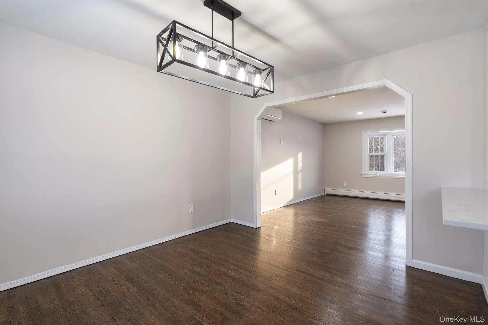 Unfurnished dining area featuring arched walkways, dark wood finished floors, a baseboard radiator, and a wall mounted air conditioner Unfurnished dining area featuring arched walkways, dark wood finished floors, a baseboard radiator, and a wall mounted air conditioner