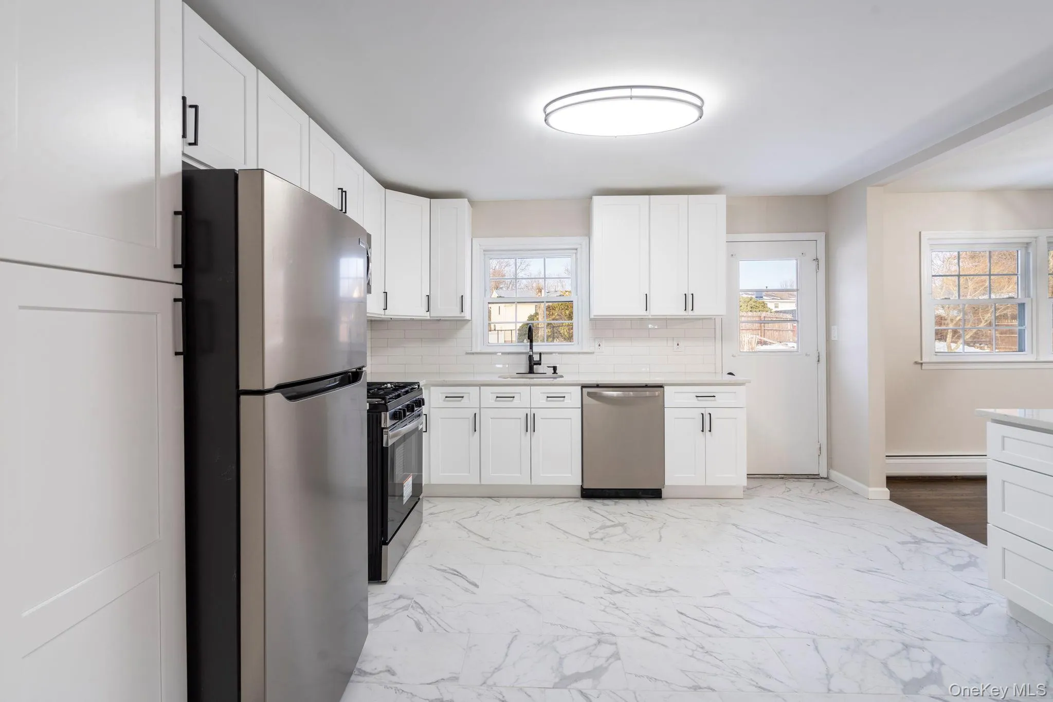 Kitchen featuring light marble finish flooring, appliances with stainless steel finishes, white cabinets, and tasteful backsplash Kitchen featuring light marble finish flooring, appliances with stainless steel finishes, white cabinets, and tasteful backsplash