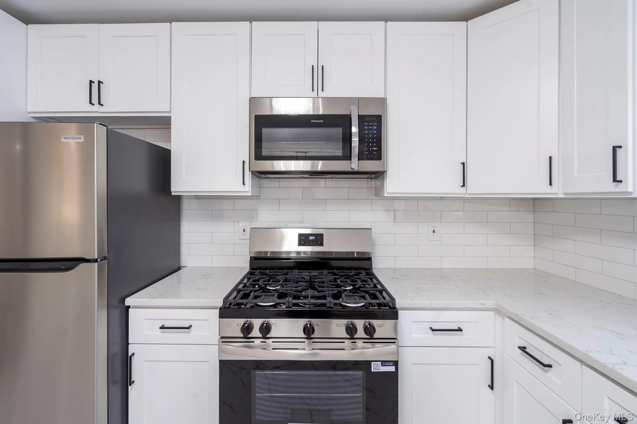Kitchen with stainless steel appliances, white cabinets, light stone counters, and backsplash Kitchen with stainless steel appliances, white cabinets, light stone counters, and backsplash