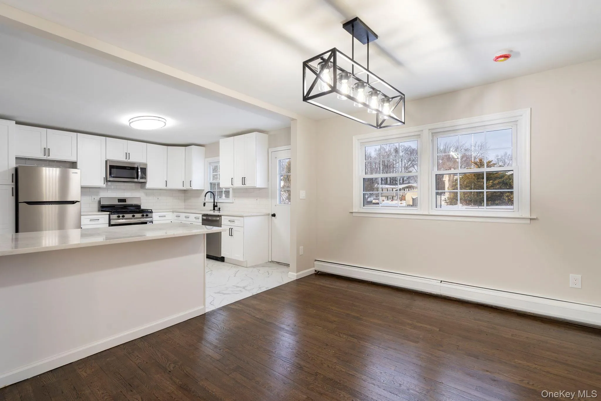 Kitchen featuring stainless steel appliances, pendant lighting, white cabinetry, a baseboard radiator, and light stone counters Kitchen featuring stainless steel appliances, pendant lighting, white cabinetry, a baseboard radiator, and light stone counters