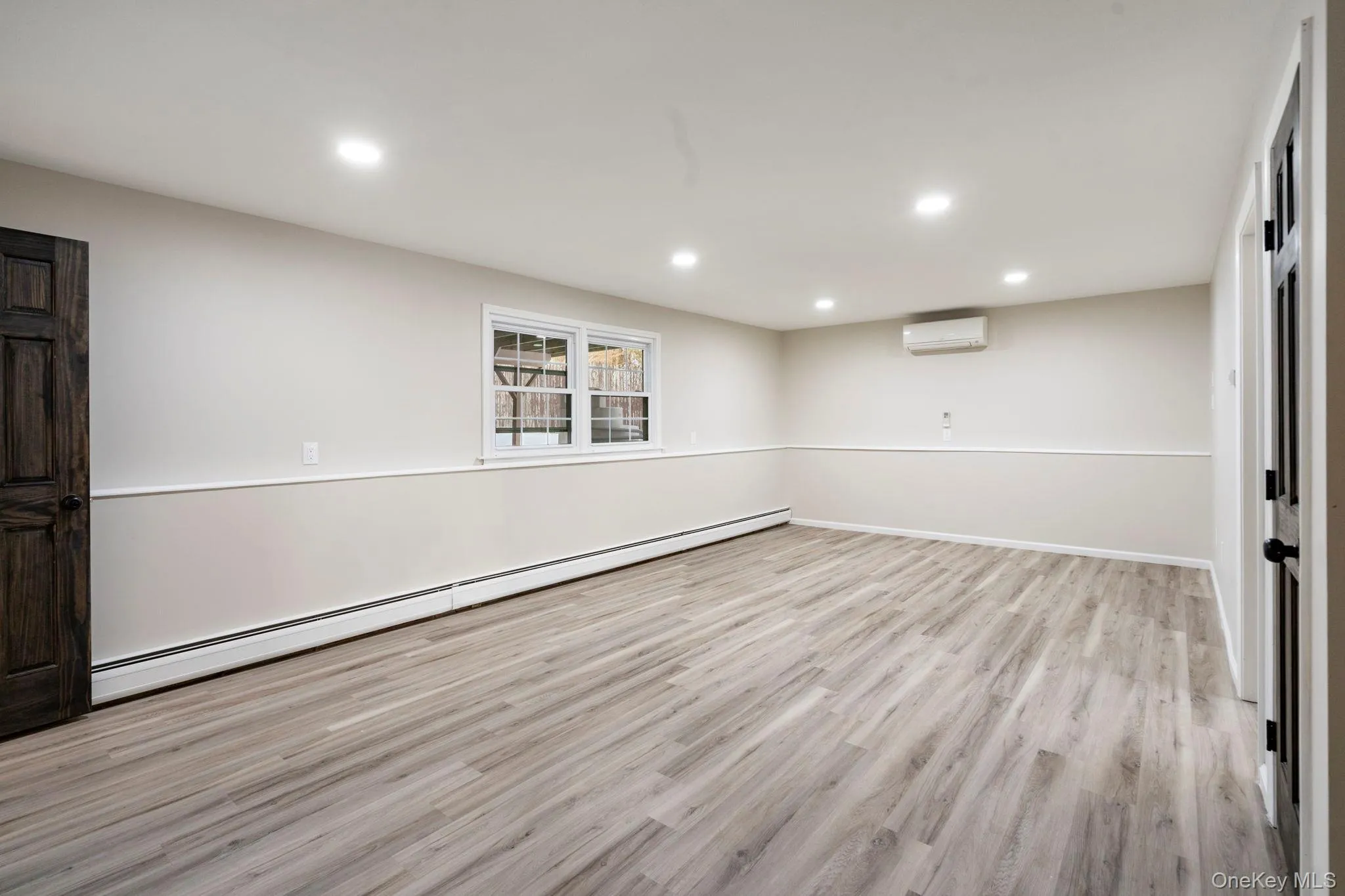 Empty room with baseboard heating, light wood-type flooring, recessed lighting, and an AC wall unit Empty room with baseboard heating, light wood-type flooring, recessed lighting, and an AC wall unit