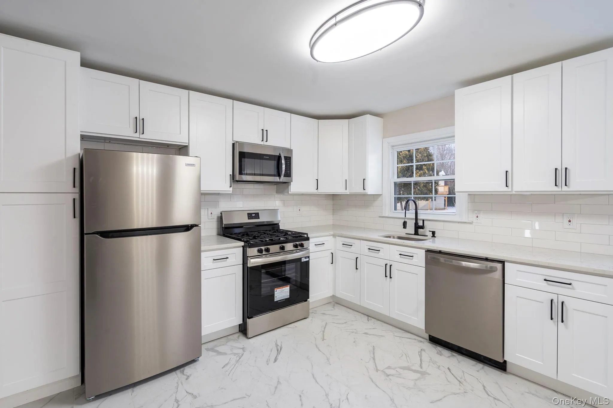 Kitchen with light marble finish flooring, appliances with stainless steel finishes, white cabinets, tasteful backsplash, and light stone counters Kitchen with light marble finish flooring, appliances with stainless steel finishes, white cabinets, tasteful backsplash, and light stone counters