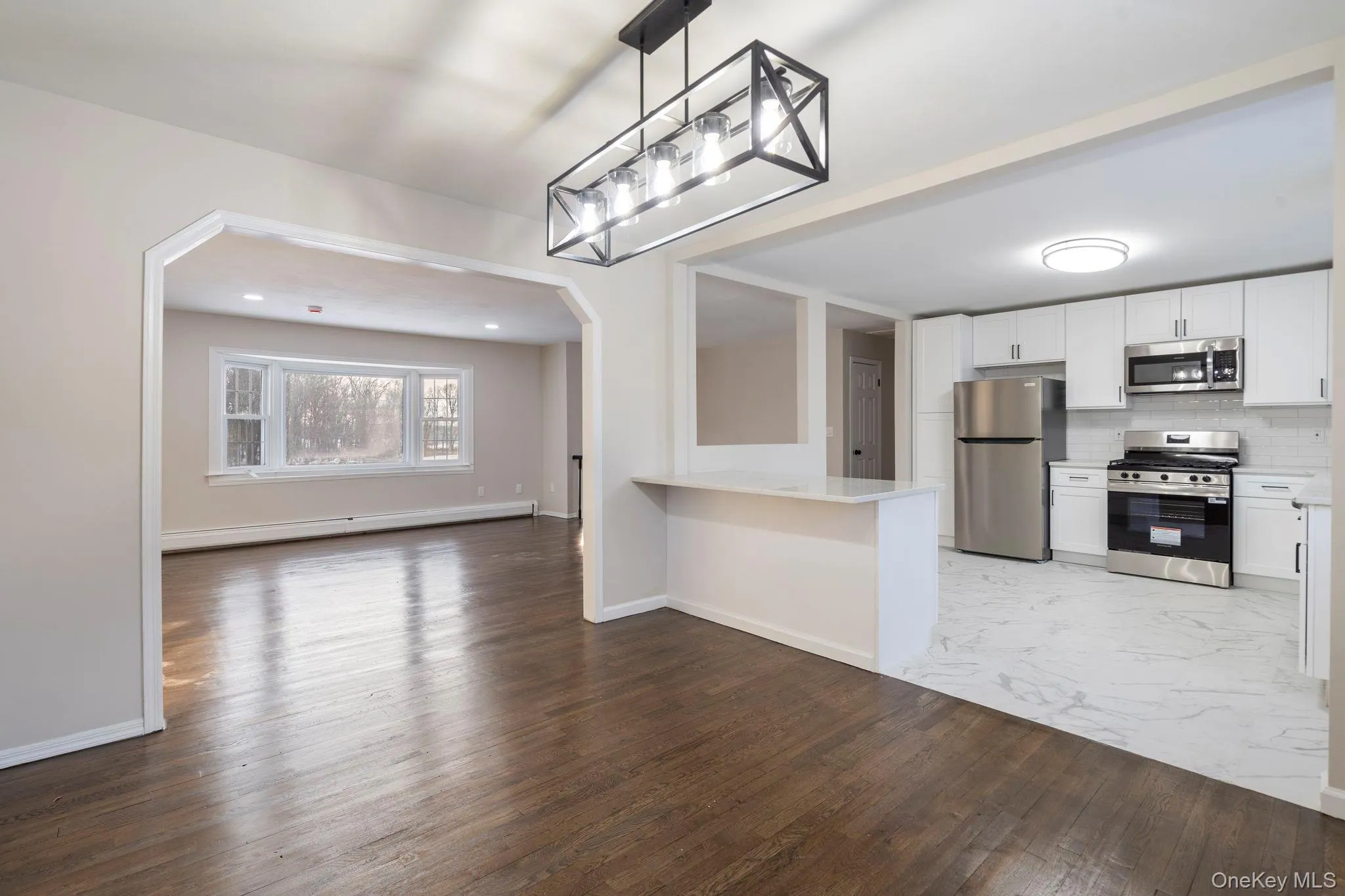 Kitchen with arched walkways, open floor plan, pendant lighting, stainless steel appliances, and white cabinets Kitchen with arched walkways, open floor plan, pendant lighting, stainless steel appliances, and white cabinets