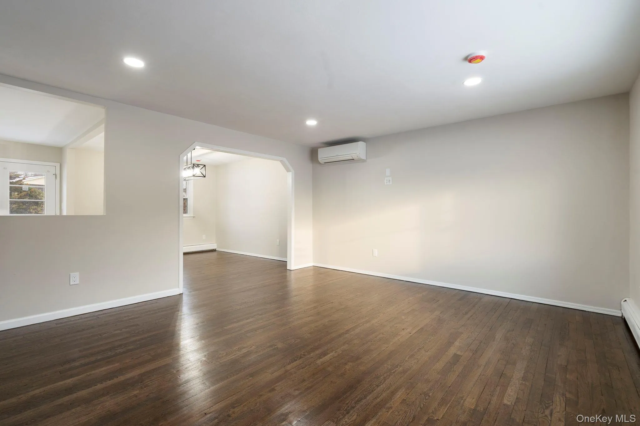 Empty room featuring arched walkways, dark wood-style floors, recessed lighting, a wall unit AC, and a baseboard radiator Empty room featuring arched walkways, dark wood-style floors, recessed lighting, a wall unit AC, and a baseboard radiator