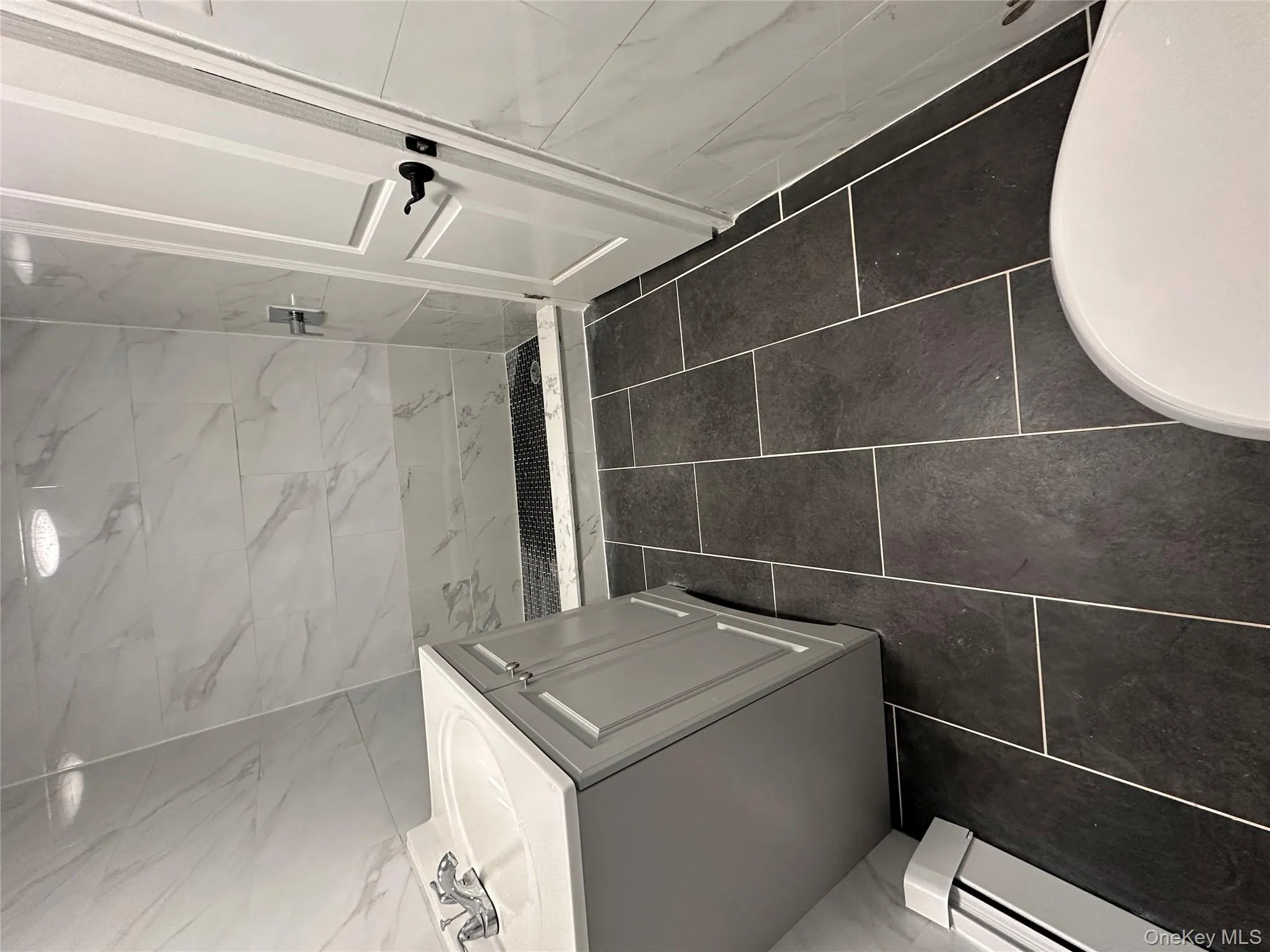 Full bath featuring a marble finish shower, dark tile patterned floors, vanity, and tile walls Full bath featuring a marble finish shower, dark tile patterned floors, vanity, and tile walls