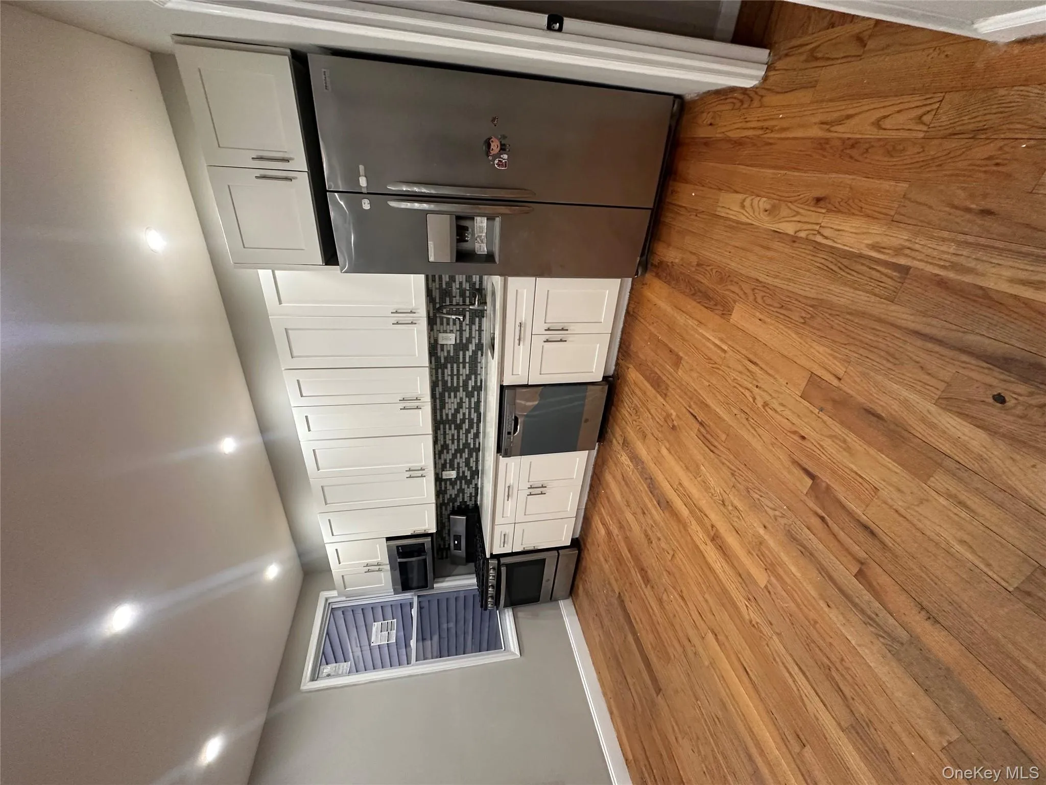 Kitchen featuring white cabinetry, stainless steel appliances, tasteful backsplash, and light wood-type flooring Kitchen featuring white cabinetry, stainless steel appliances, tasteful backsplash, and light wood-type flooring