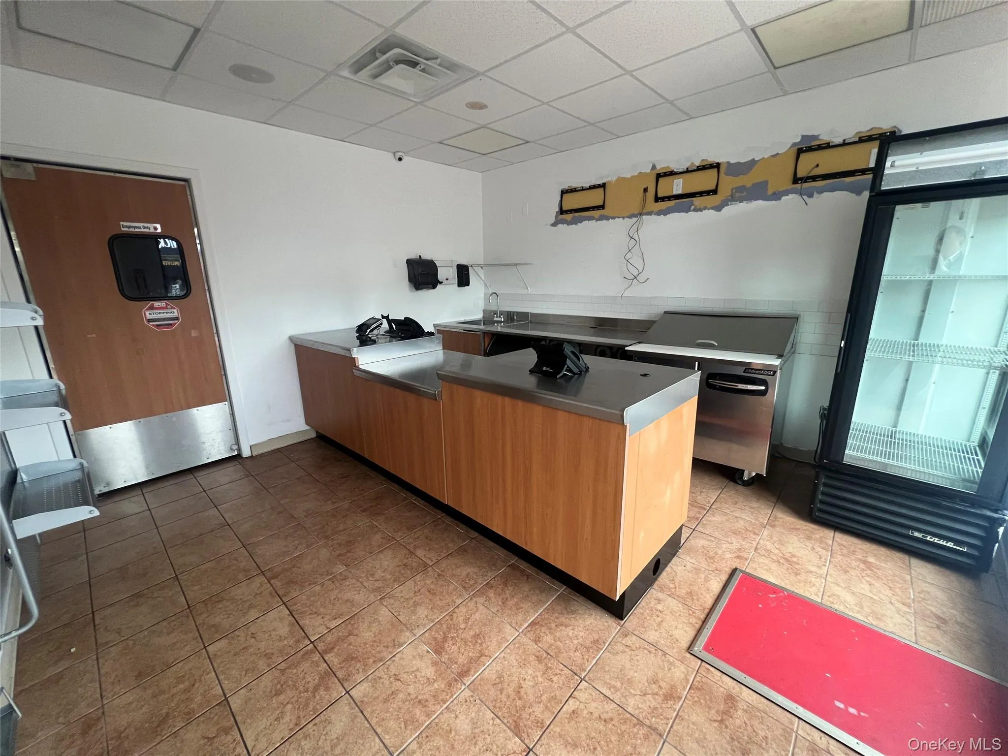 Kitchen featuring stainless steel counters, a drop ceiling, a peninsula, and fridge Kitchen featuring stainless steel counters, a drop ceiling, a peninsula, and fridge