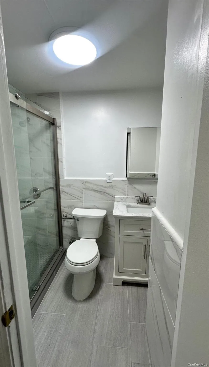 Bathroom with wainscoting, vanity, tile walls, and a stall shower Bathroom with wainscoting, vanity, tile walls, and a stall shower