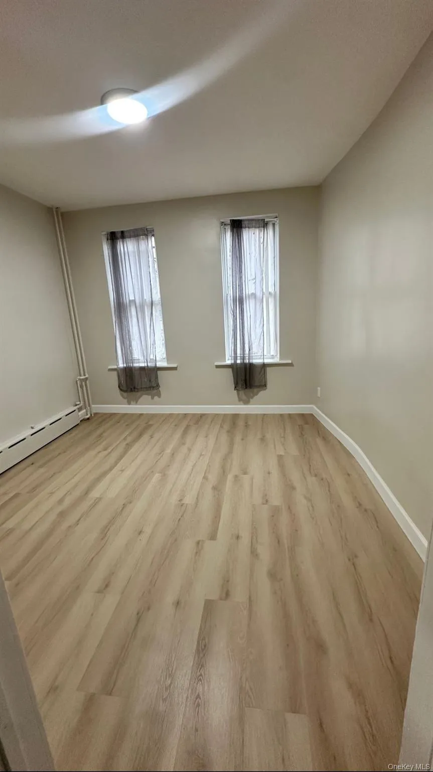 Empty room featuring light wood-style flooring, a baseboard heating unit, and healthy amount of natural light Empty room featuring light wood-style flooring, a baseboard heating unit, and healthy amount of natural light