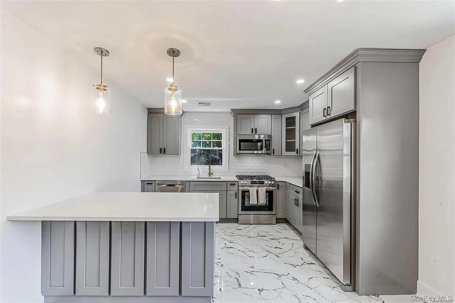 Kitchen featuring gray cabinets, a peninsula, light marble finish flooring, appliances with stainless steel finishes, and recessed lighting Kitchen featuring gray cabinets, a peninsula, light marble finish flooring, appliances with stainless steel finishes, and recessed lighting