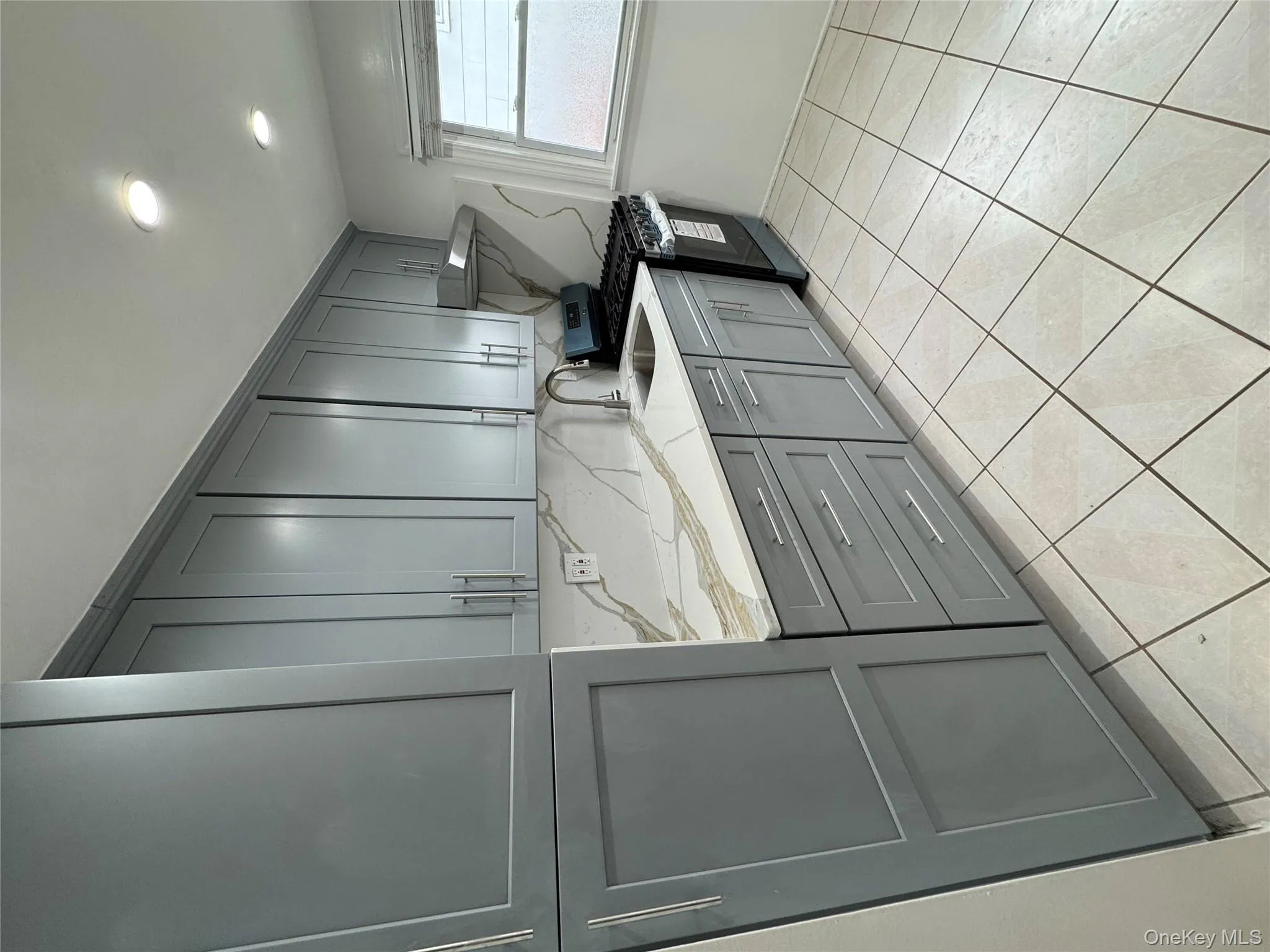 Kitchen featuring gray cabinets, stove, light stone countertops, tasteful backsplash, and range hood Kitchen featuring gray cabinets, stove, light stone countertops, tasteful backsplash, and range hood