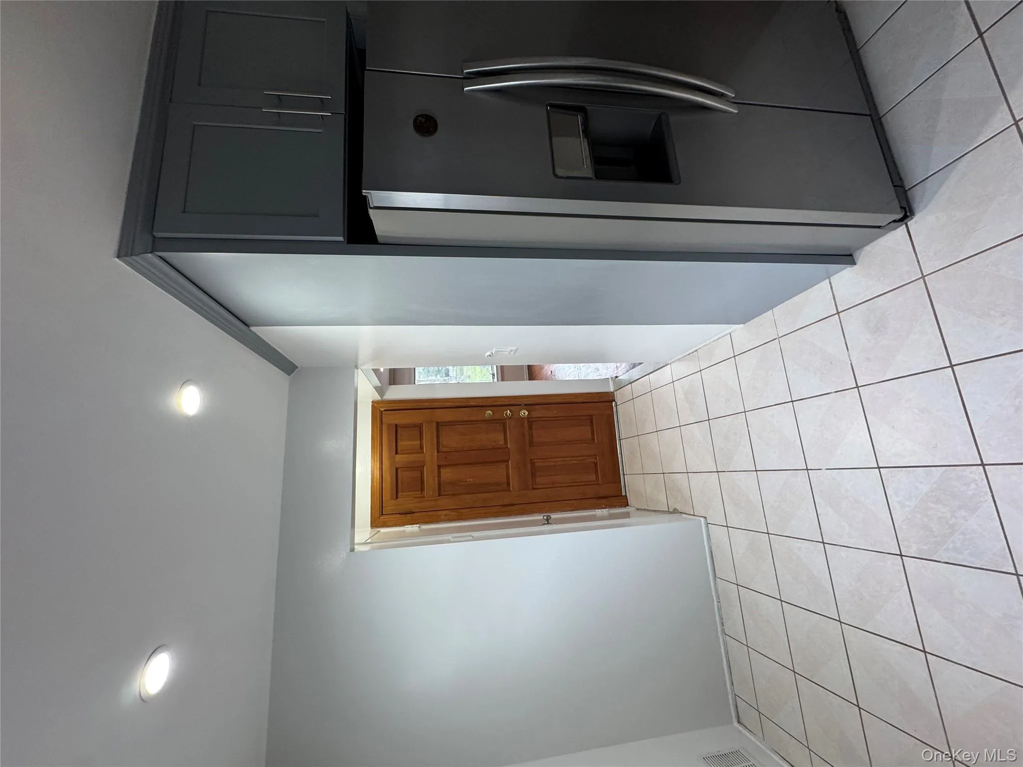 Kitchen with fridge, light tile patterned floors, recessed lighting, and gray cabinetry Kitchen with fridge, light tile patterned floors, recessed lighting, and gray cabinetry