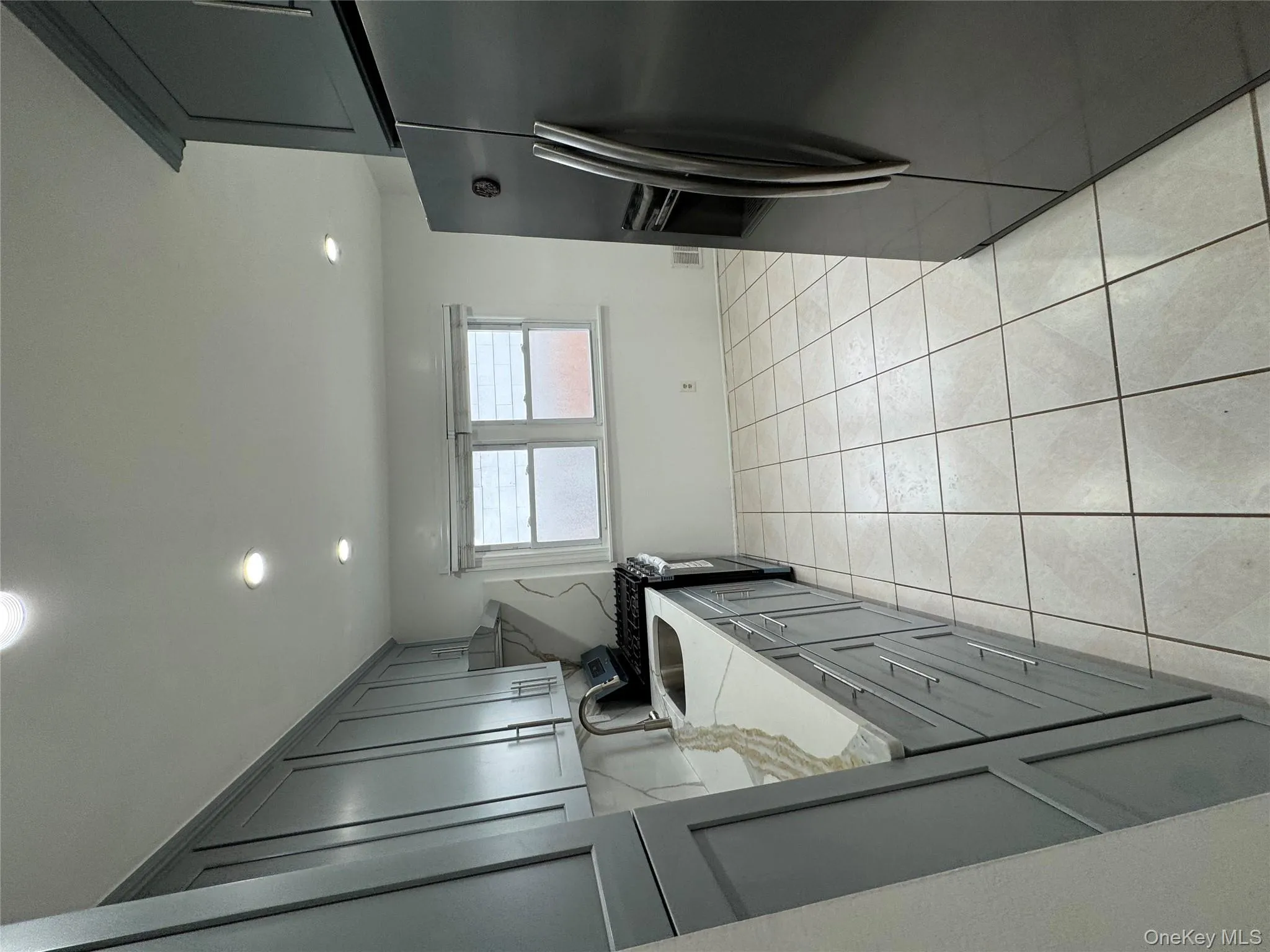 Kitchen featuring fridge, stove, light stone counters, gray cabinetry, and light tile patterned floors Kitchen featuring fridge, stove, light stone counters, gray cabinetry, and light tile patterned floors