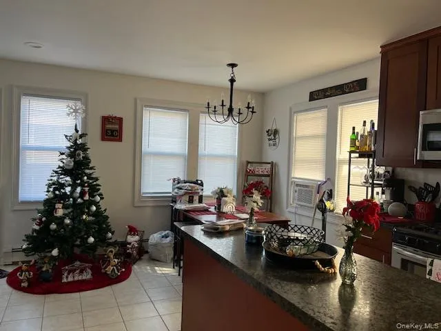 Kitchen featuring dark countertops, light tile patterned floors, pendant lighting, a chandelier, and appliances with stainless steel finishes Kitchen featuring dark countertops, light tile patterned floors, pendant lighting, a chandelier, and appliances with stainless steel finishes