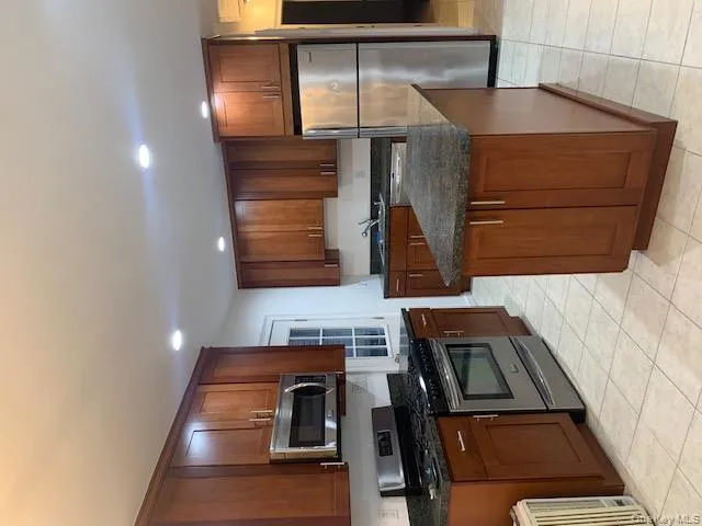 Kitchen featuring stainless steel refrigerator, range, recessed lighting, light tile patterned floors, and brown cabinetry Kitchen featuring stainless steel refrigerator, range, recessed lighting, light tile patterned floors, and brown cabinetry