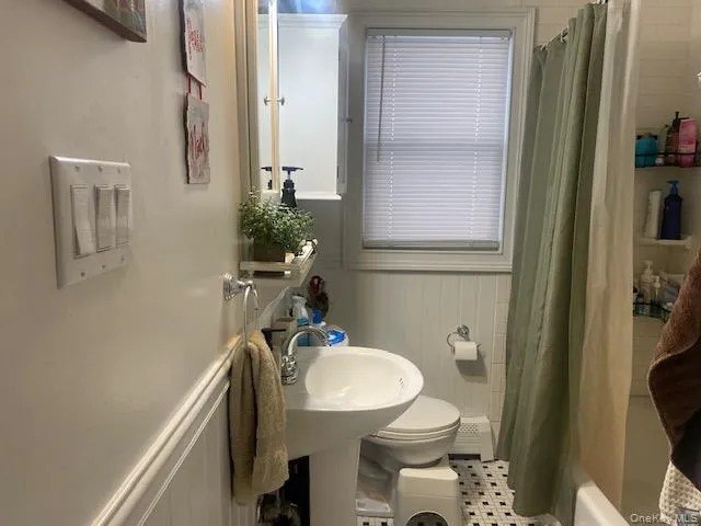 Full bathroom with shower / bath combo with shower curtain, a baseboard radiator, and wainscoting Full bathroom with shower / bath combo with shower curtain, a baseboard radiator, and wainscoting