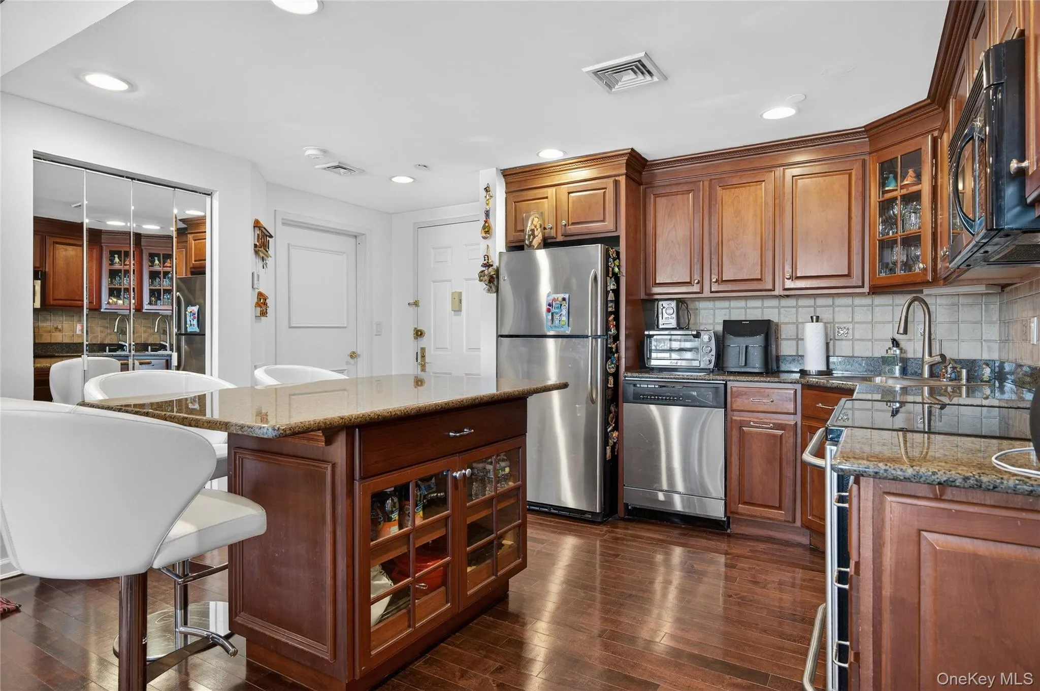 Kitchen with glass insert cabinets, decorative backsplash, a breakfast bar, stainless steel appliances, and dark stone counters Kitchen with glass insert cabinets, decorative backsplash, a breakfast bar, stainless steel appliances, and dark stone counters