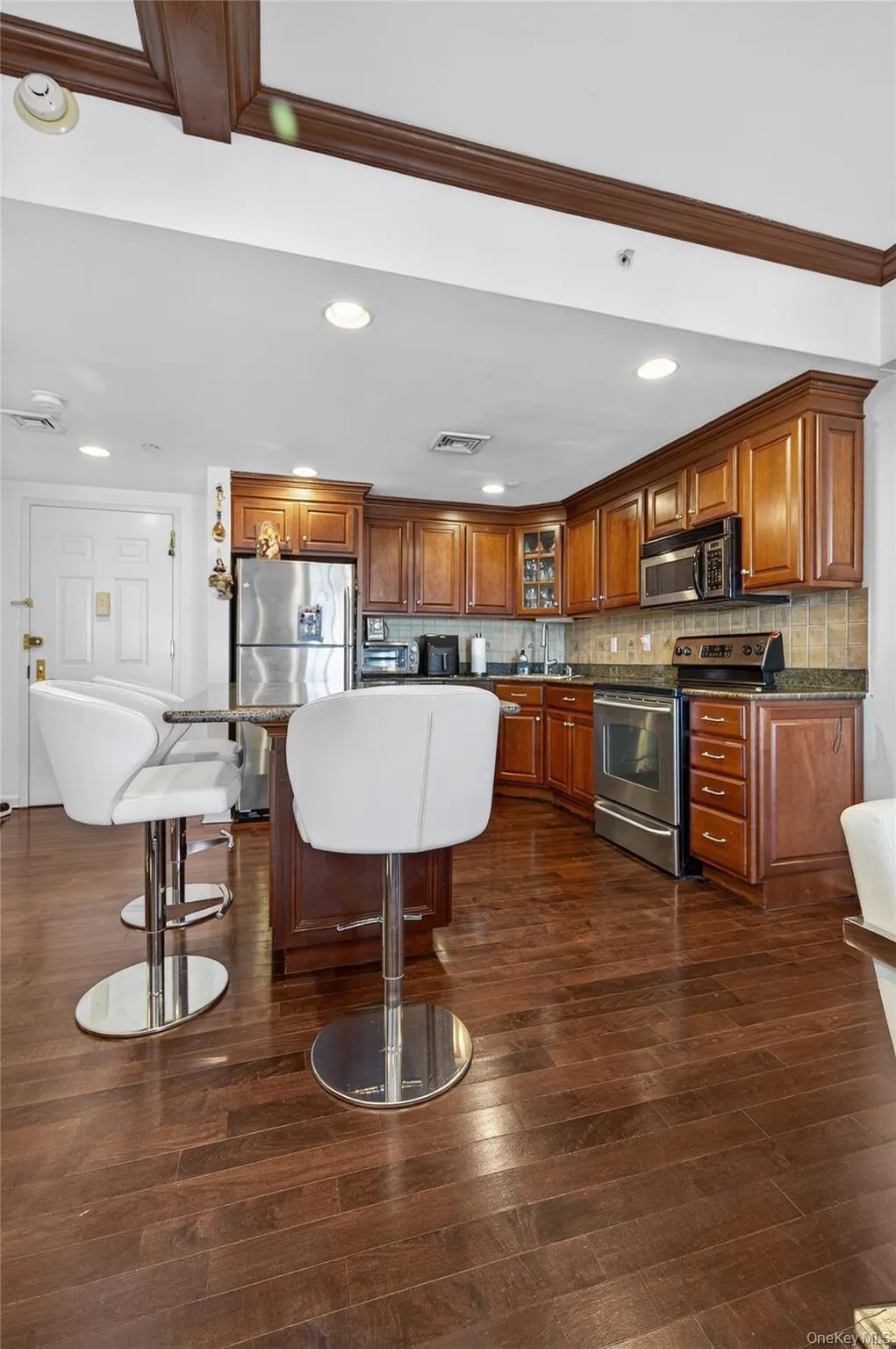 Kitchen featuring stainless steel appliances, glass insert cabinets, a kitchen bar, brown cabinets, and recessed lighting Kitchen featuring stainless steel appliances, glass insert cabinets, a kitchen bar, brown cabinets, and recessed lighting