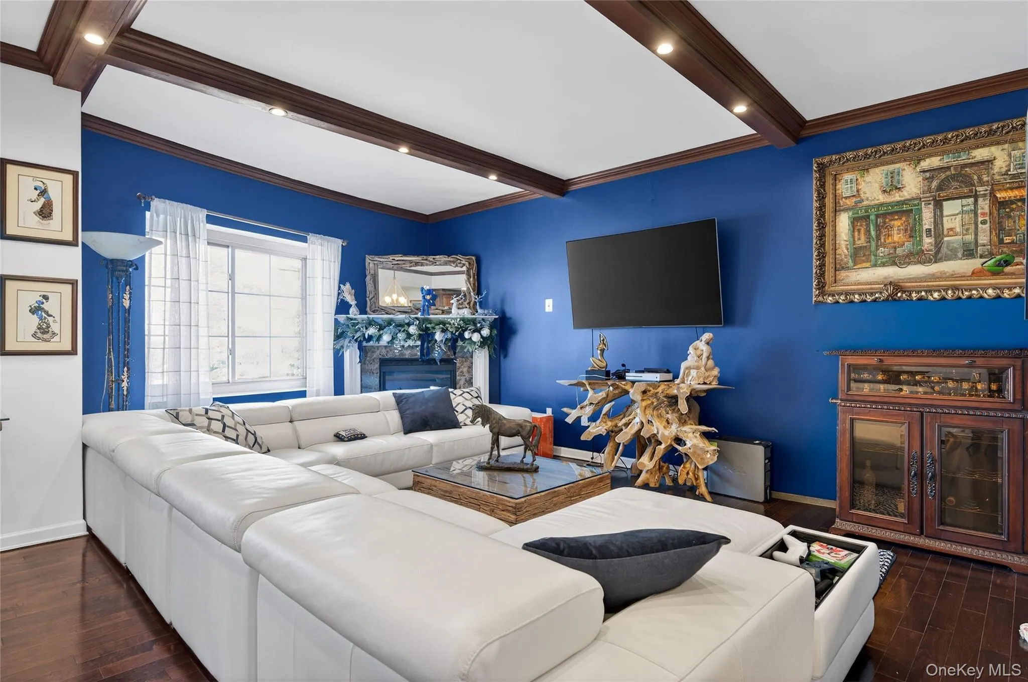 Living area with dark wood-type flooring, a high end fireplace, ornamental molding, and beamed ceiling Living area with dark wood-type flooring, a high end fireplace, ornamental molding, and beamed ceiling