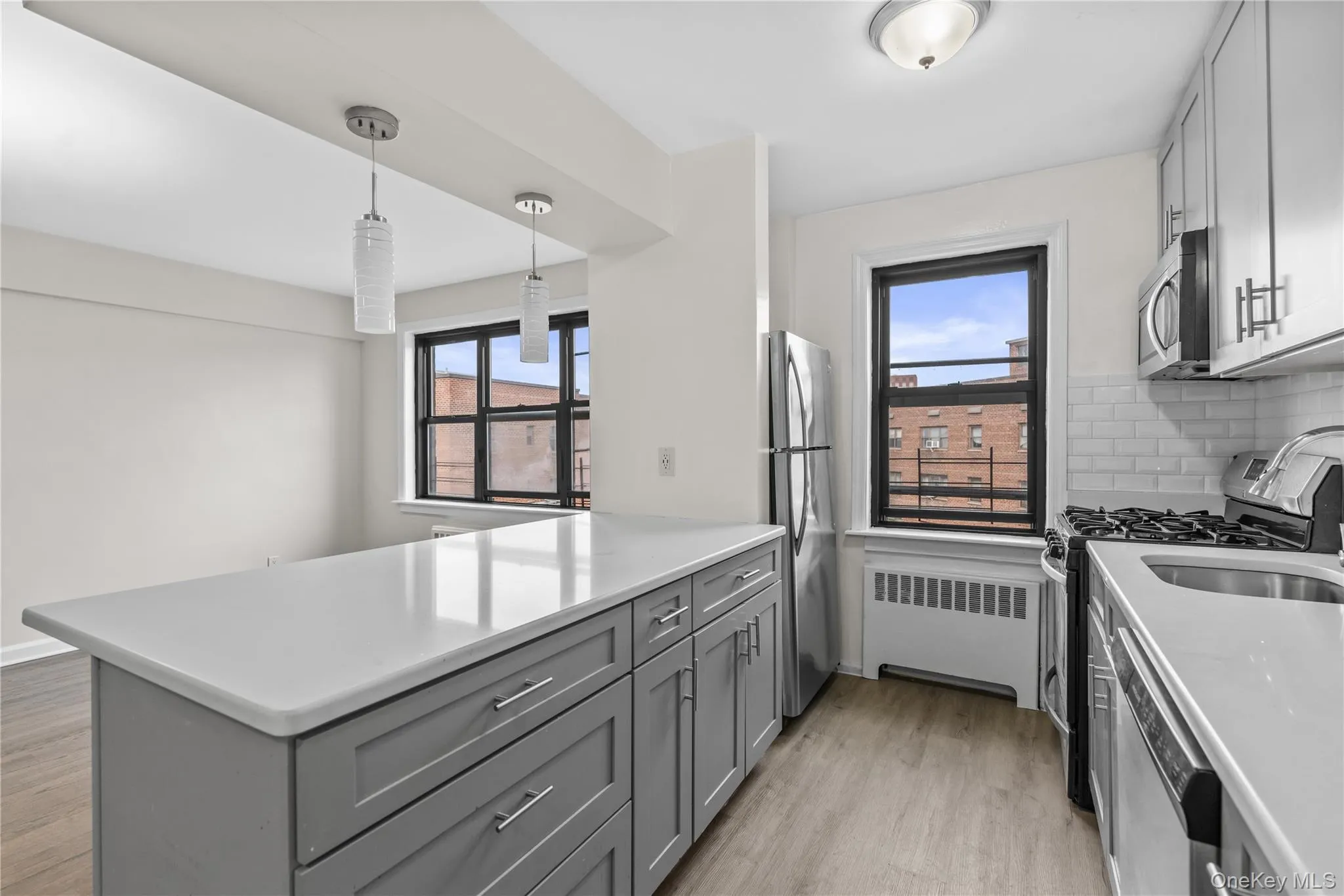 Kitchen featuring gray cabinetry, stainless steel appliances, pendant lighting, radiator heating unit, and a peninsula Kitchen featuring gray cabinetry, stainless steel appliances, pendant lighting, radiator heating unit, and a peninsula