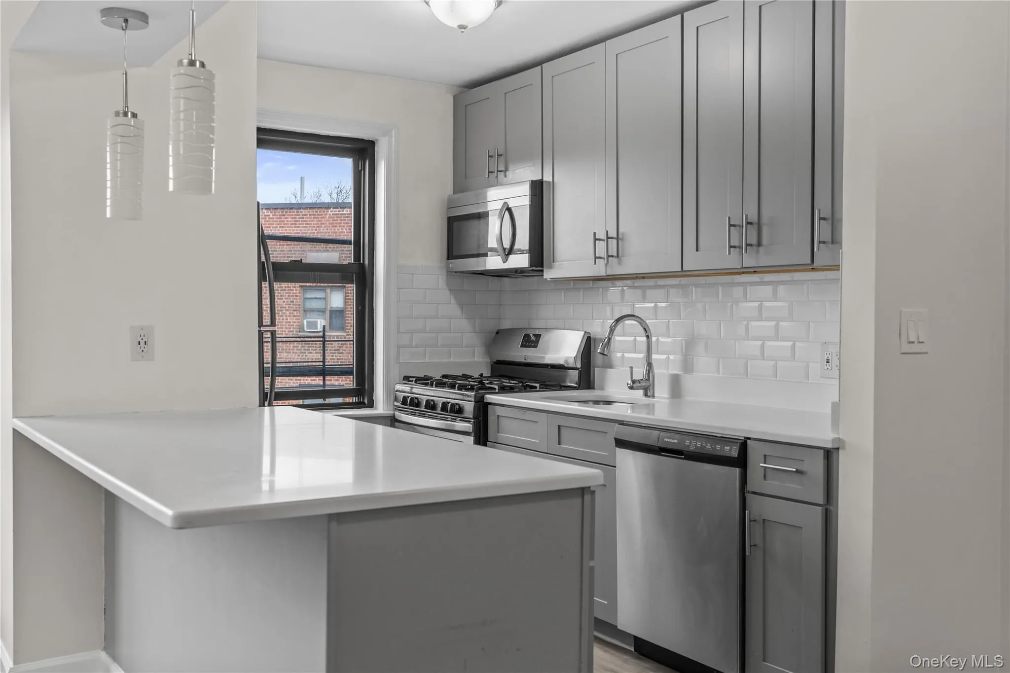 Kitchen featuring stainless steel appliances, pendant lighting, gray cabinetry, a peninsula, and decorative backsplash Kitchen featuring stainless steel appliances, pendant lighting, gray cabinetry, a peninsula, and decorative backsplash