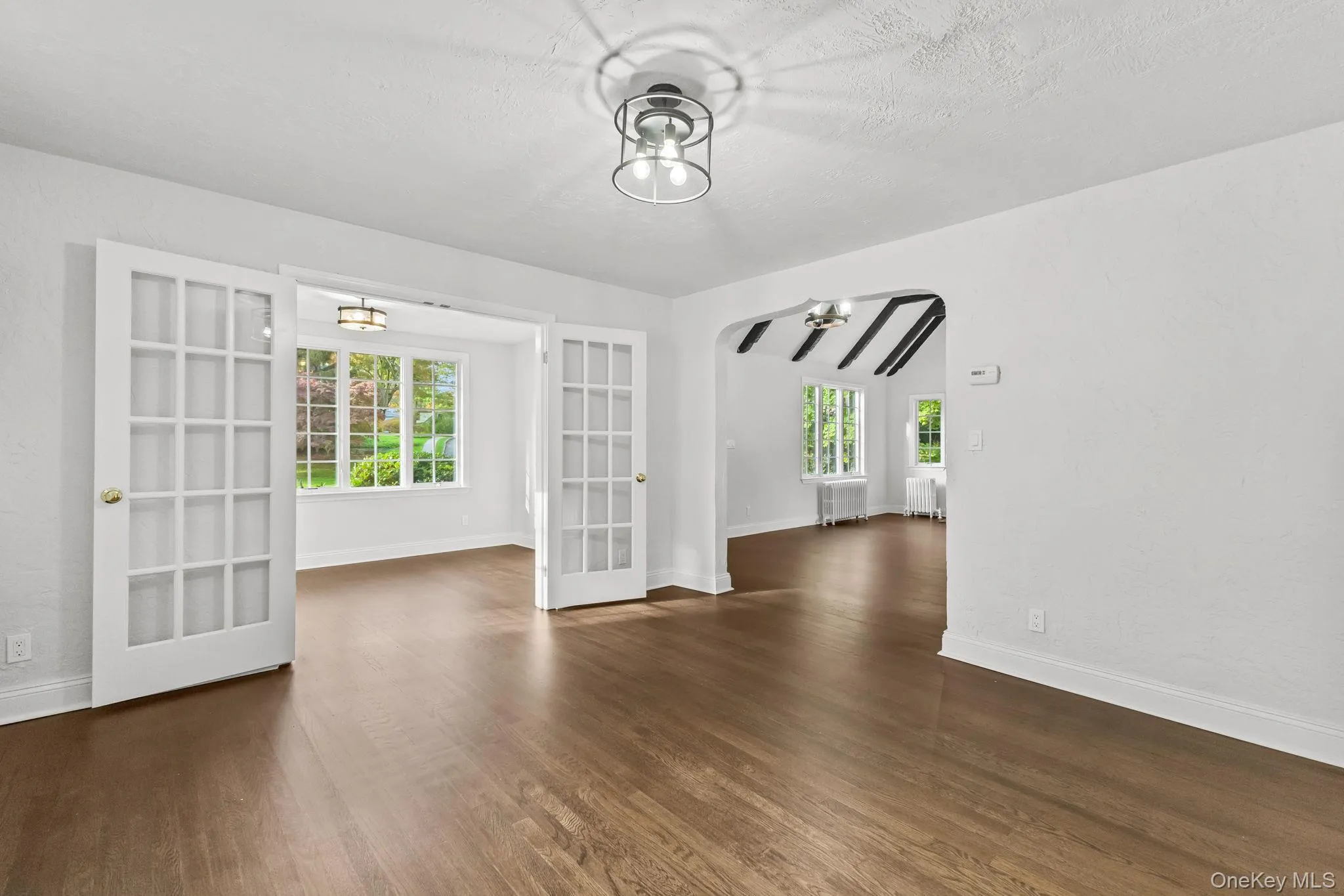 Unfurnished room with healthy amount of natural light, dark wood-style flooring, radiator heating unit, french doors, and a textured ceiling Unfurnished room with healthy amount of natural light, dark wood-style flooring, radiator heating unit, french doors, and a textured ceiling