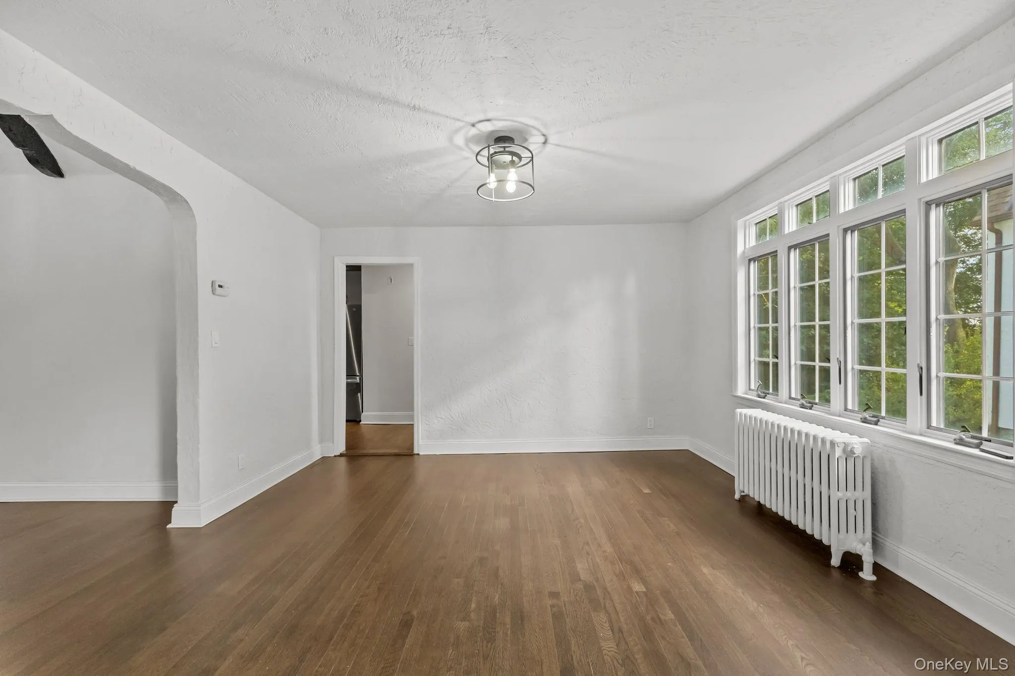 Unfurnished room with radiator, dark wood-type flooring, a textured ceiling, and arched walkways Unfurnished room with radiator, dark wood-type flooring, a textured ceiling, and arched walkways