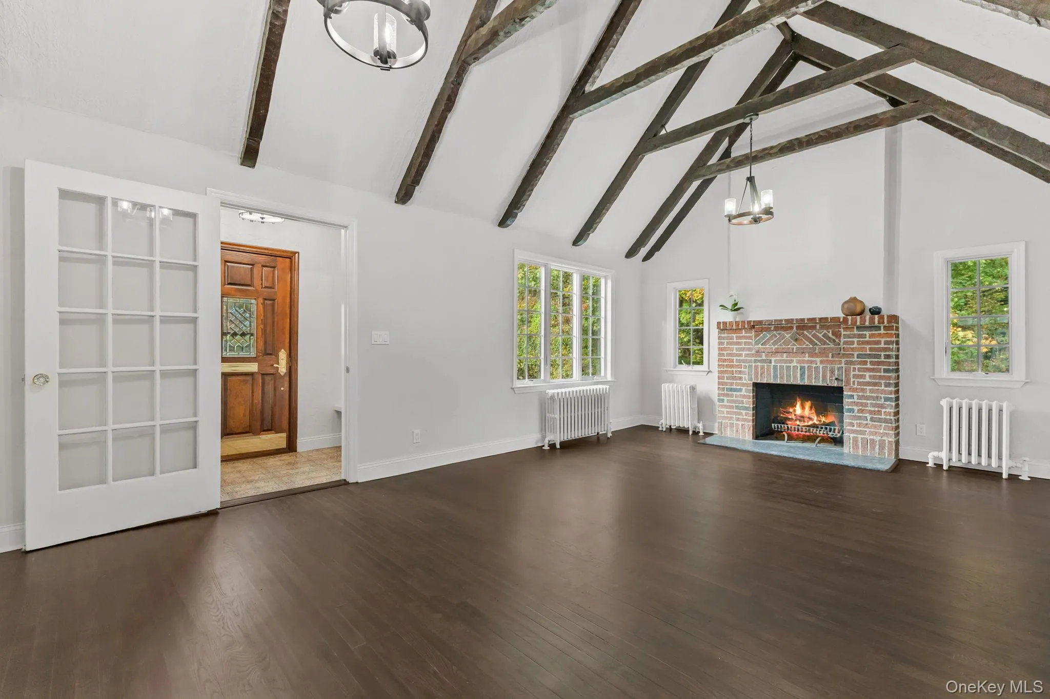 living room with a chandelier, high vaulted ceiling, dark wood-type flooring, and a brick fireplace living room with a chandelier, high vaulted ceiling, dark wood-type flooring, and a brick fireplace
