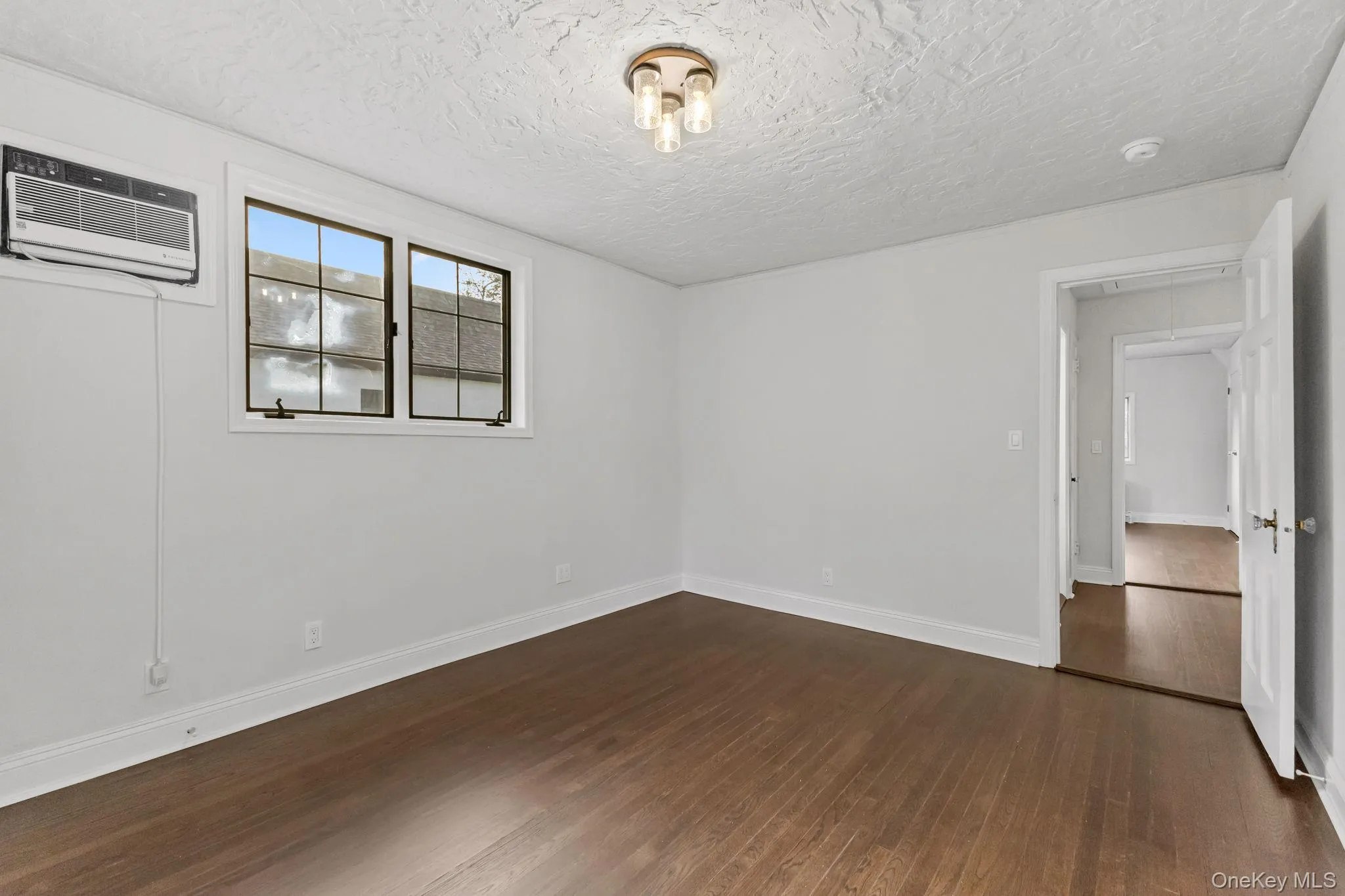 Unfurnished bedroom featuring dark wood-type flooring, attic access, a textured ceiling, and a wall unit AC Unfurnished bedroom featuring dark wood-type flooring, attic access, a textured ceiling, and a wall unit AC