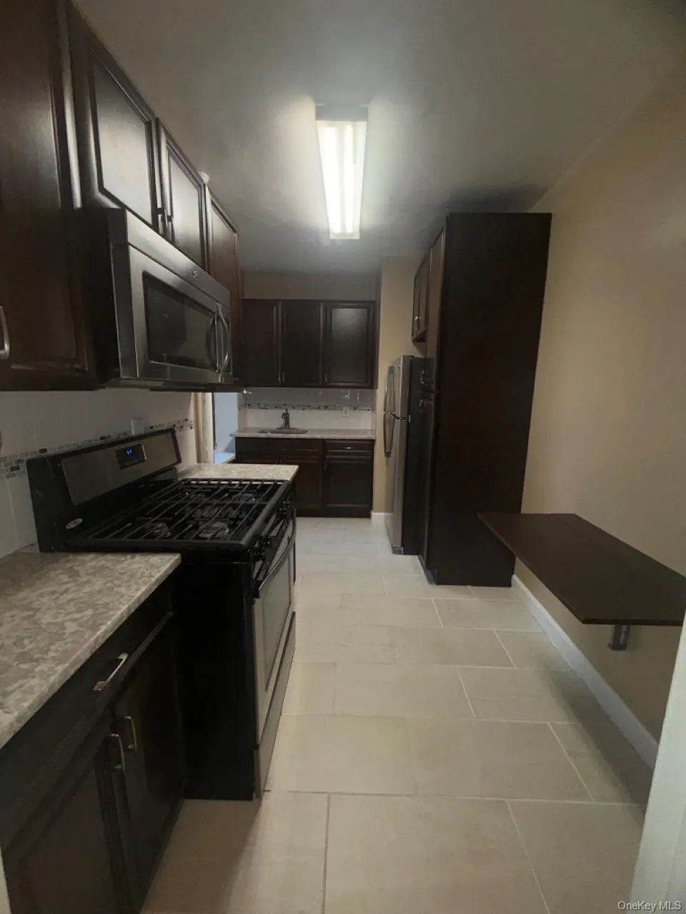 Kitchen featuring appliances with stainless steel finishes, dark brown cabinetry, and light tile patterned floors Kitchen featuring appliances with stainless steel finishes, dark brown cabinetry, and light tile patterned floors
