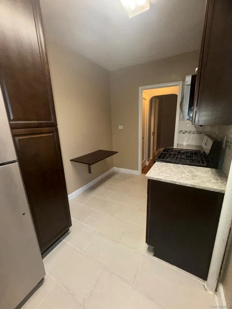 Kitchen with dark brown cabinets, appliances with stainless steel finishes, light tile patterned flooring, and light stone counters Kitchen with dark brown cabinets, appliances with stainless steel finishes, light tile patterned flooring, and light stone counters