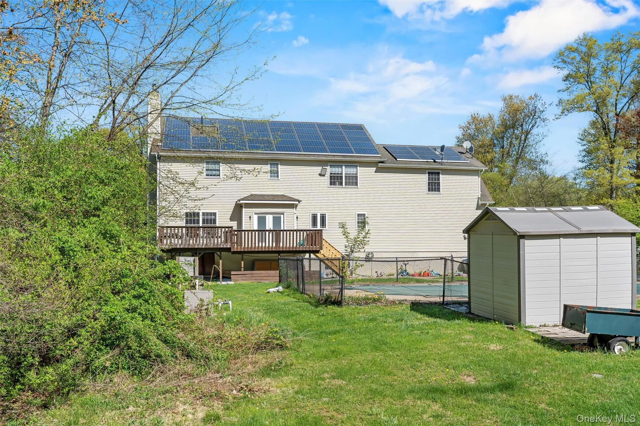Back of house with a storage unit, roof mounted solar panels, a wooden deck, a chimney, and a fenced backyard Back of house with a storage unit, roof mounted solar panels, a wooden deck, a chimney, and a fenced backyard