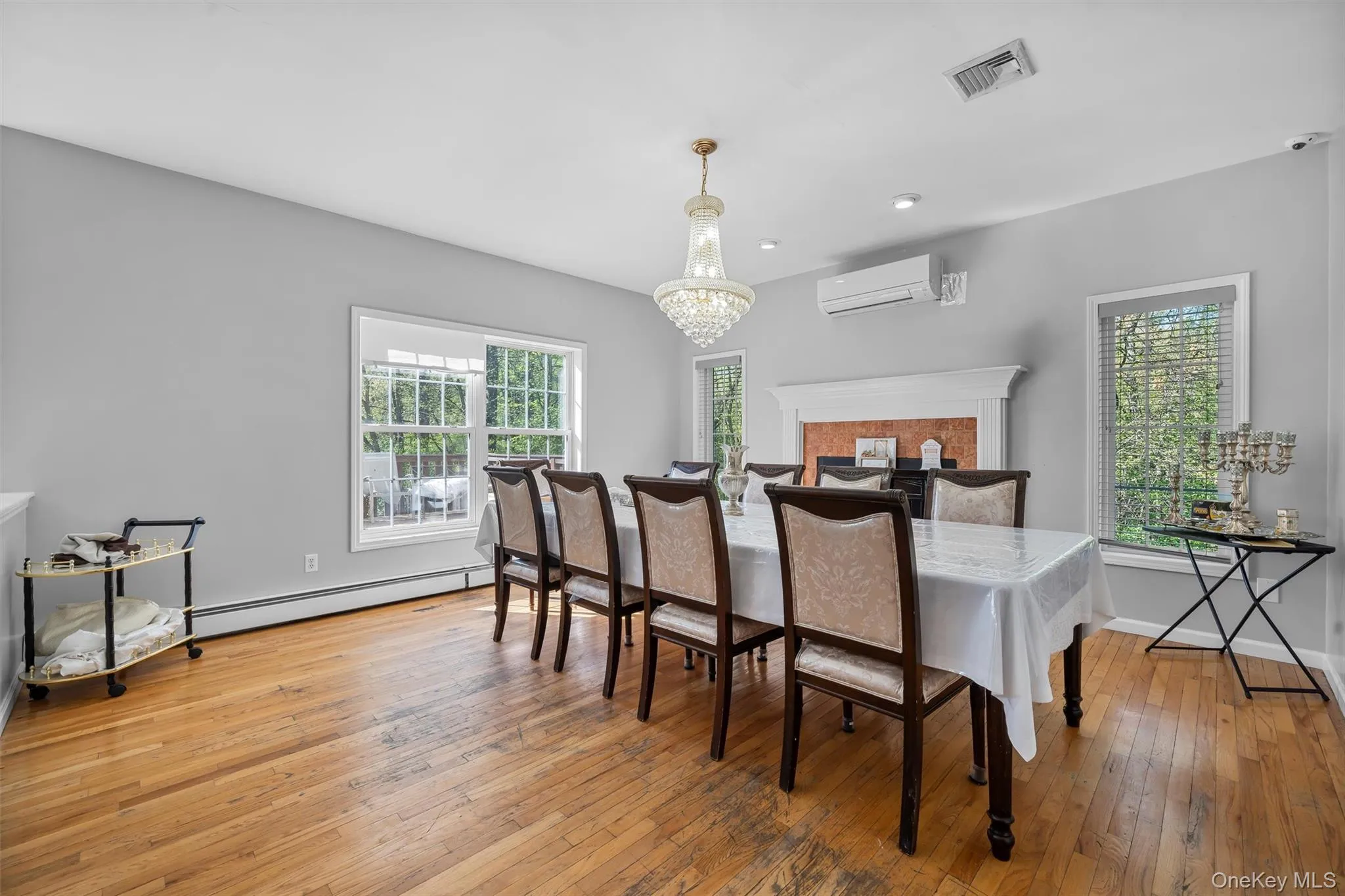 Dining area featuring light wood-type flooring, a wall mounted AC, baseboard heating, a chandelier, and plenty of natural light Dining area featuring light wood-type flooring, a wall mounted AC, baseboard heating, a chandelier, and plenty of natural light