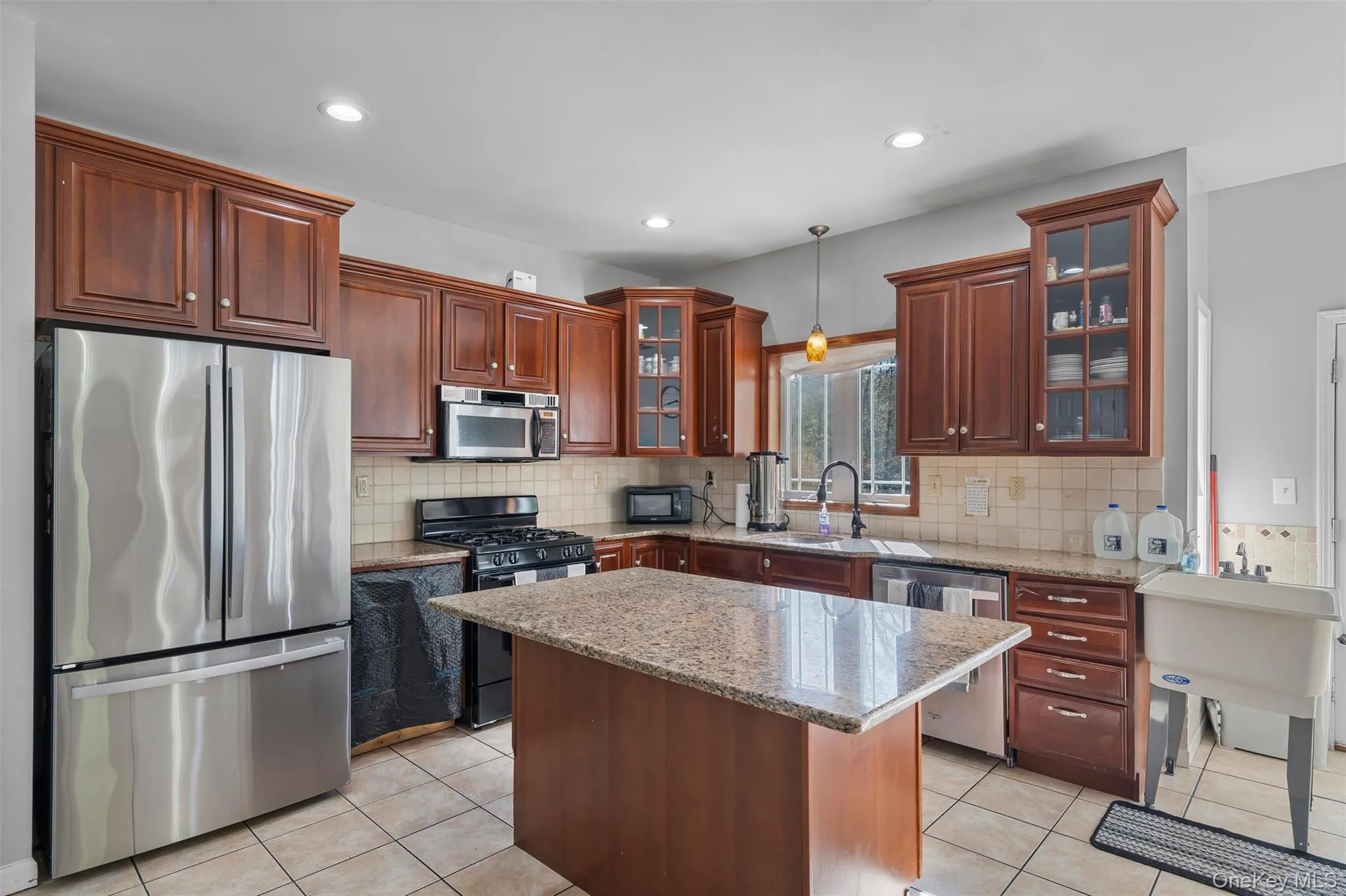 Kitchen featuring black appliances, glass insert cabinets, light stone counters, light tile patterned floors, and recessed lighting Kitchen featuring black appliances, glass insert cabinets, light stone counters, light tile patterned floors, and recessed lighting