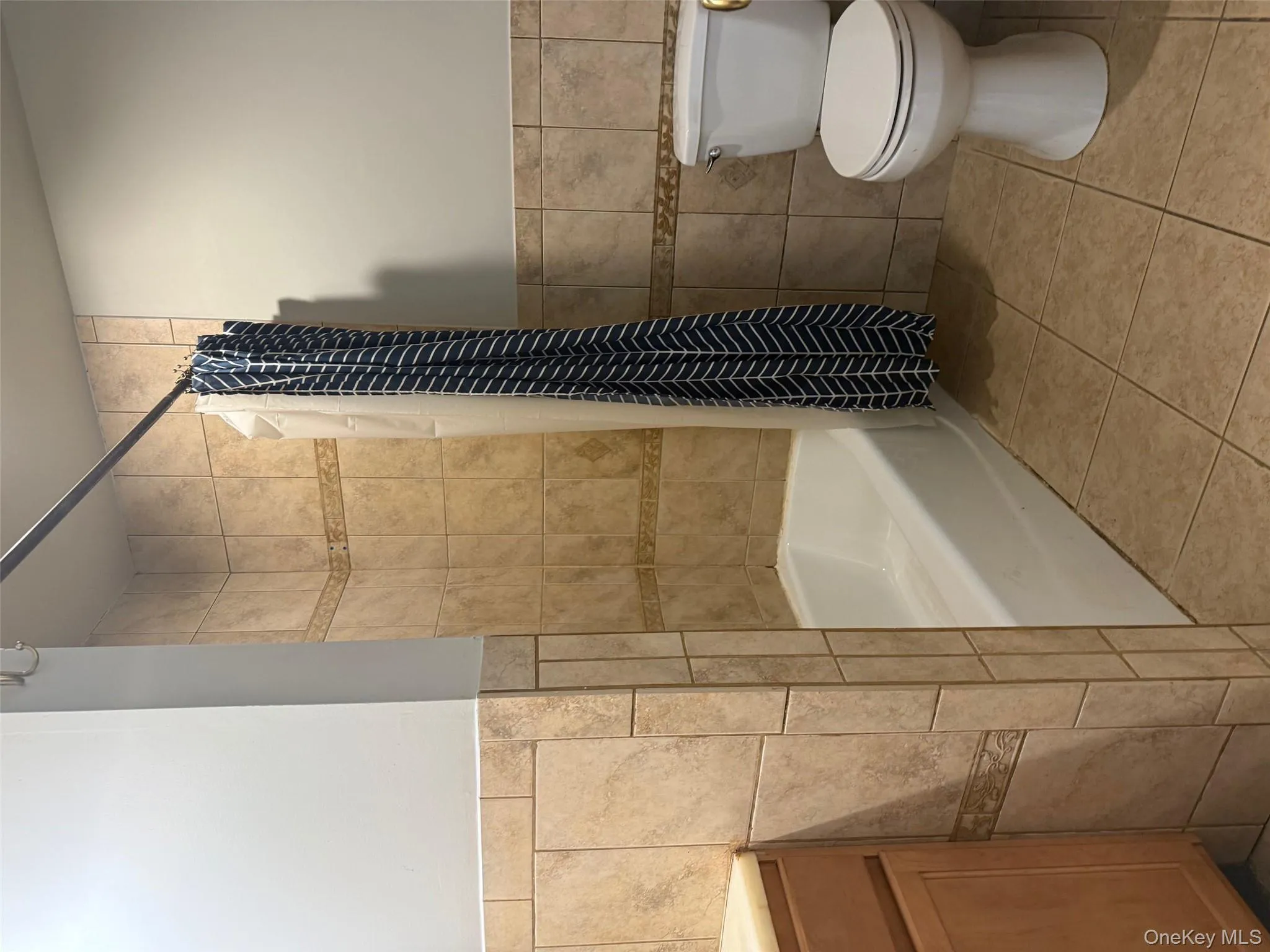Bathroom featuring tile walls, tile patterned floors, shower / tub combo with curtain, vanity, and a wainscoted wall Bathroom featuring tile walls, tile patterned floors, shower / tub combo with curtain, vanity, and a wainscoted wall
