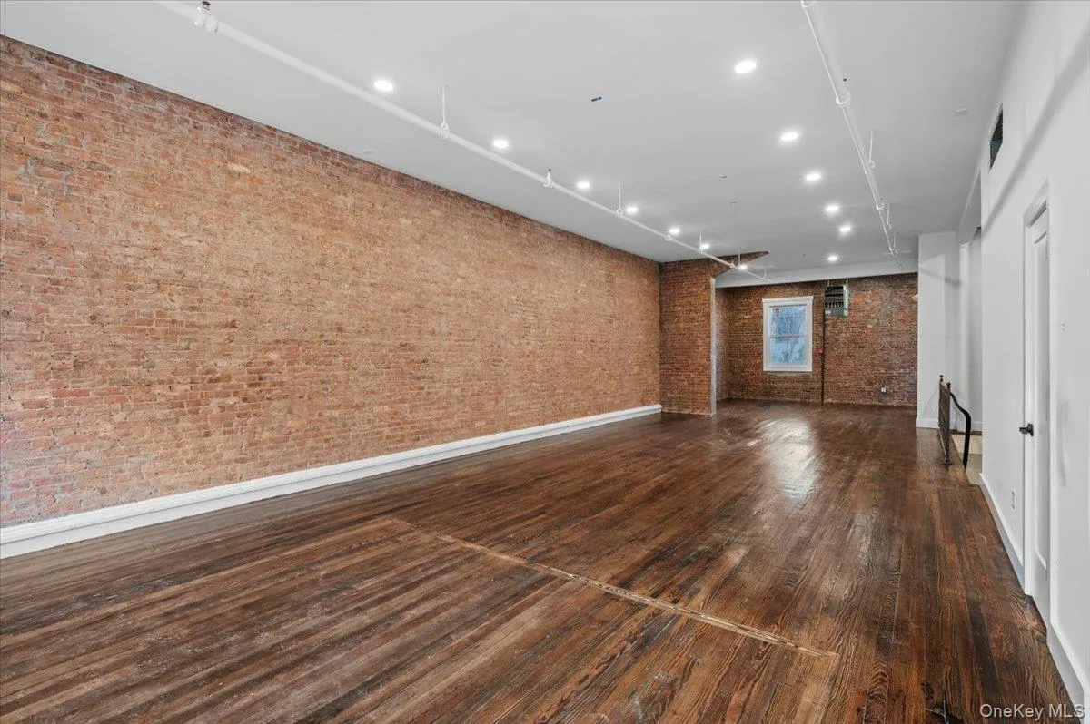 Unfurnished living room featuring recessed lighting, brick wall, and dark wood-type flooring Unfurnished living room featuring recessed lighting, brick wall, and dark wood-type flooring