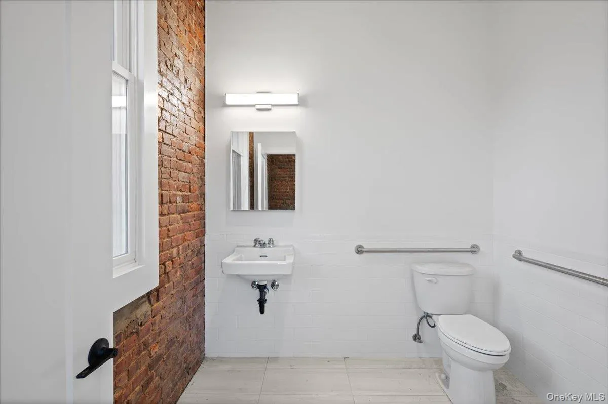 Half bathroom featuring tile walls, wainscoting, and brick wall Half bathroom featuring tile walls, wainscoting, and brick wall