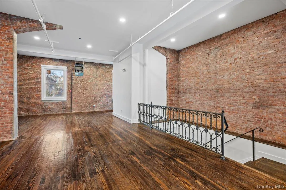 Empty room featuring brick wall, hardwood / wood-style flooring, recessed lighting, and attic access Empty room featuring brick wall, hardwood / wood-style flooring, recessed lighting, and attic access
