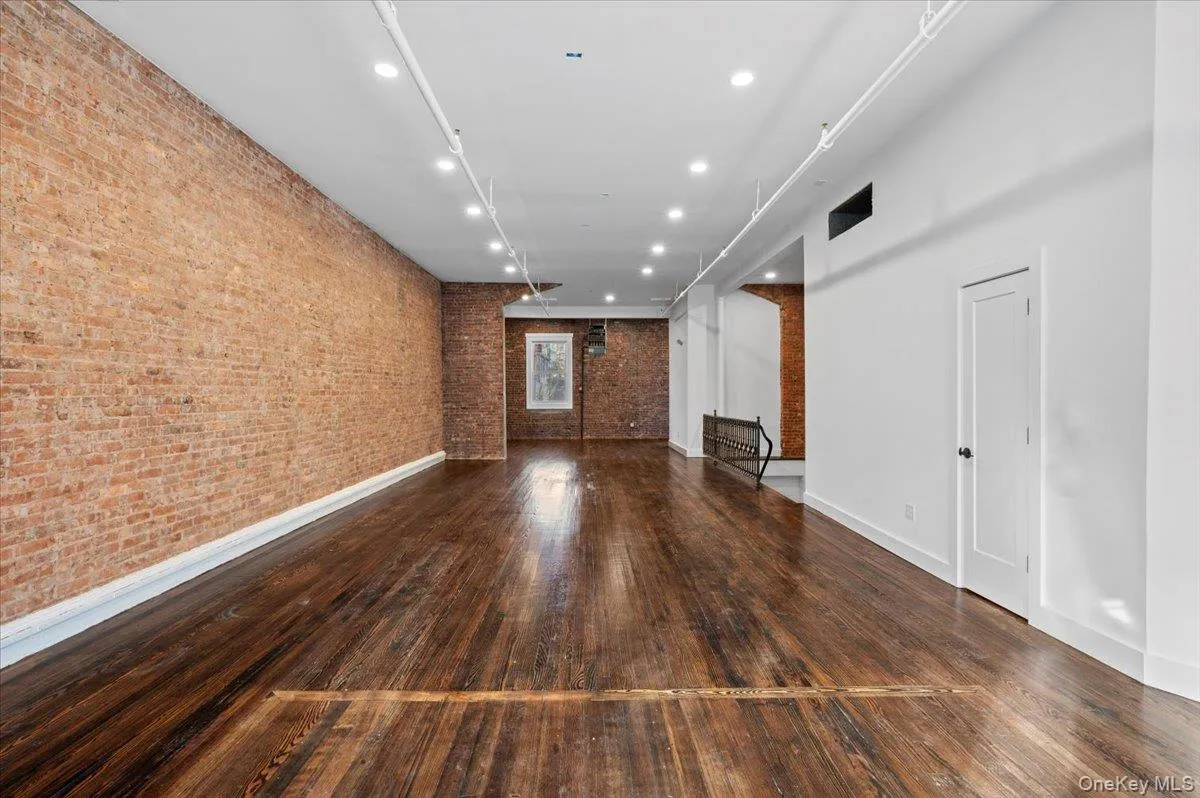 Unfurnished living room featuring dark wood-type flooring, recessed lighting, and brick wall Unfurnished living room featuring dark wood-type flooring, recessed lighting, and brick wall