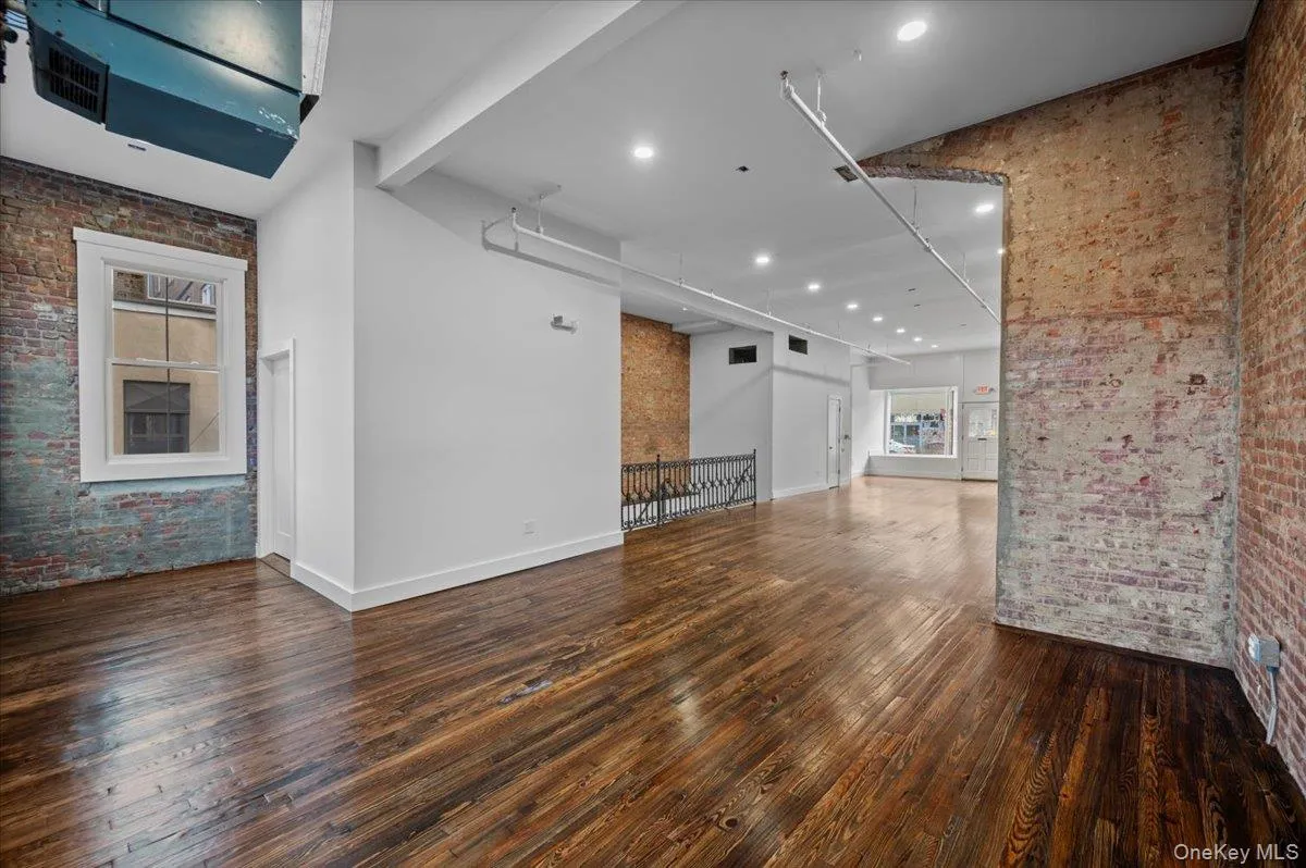 Unfurnished living room featuring brick wall, a high ceiling, dark wood-style floors, recessed lighting, and an accent wall Unfurnished living room featuring brick wall, a high ceiling, dark wood-style floors, recessed lighting, and an accent wall