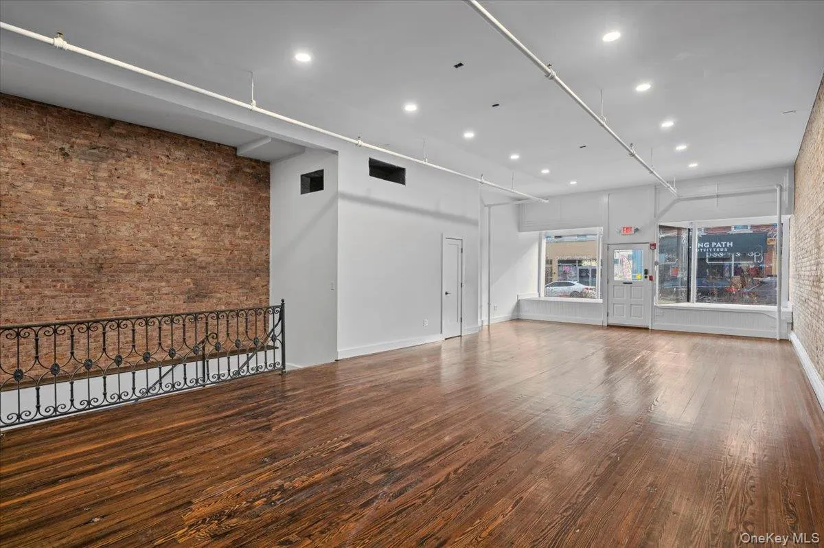 Unfurnished living room with brick wall, hardwood / wood-style floors, recessed lighting, a towering ceiling, and an accent wall Unfurnished living room with brick wall, hardwood / wood-style floors, recessed lighting, a towering ceiling, and an accent wall