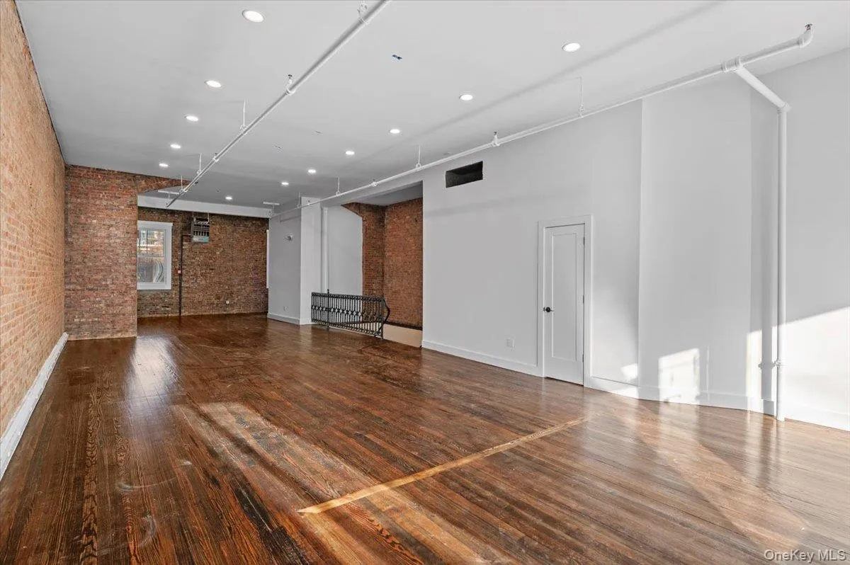Unfurnished living room featuring recessed lighting, brick wall, hardwood / wood-style floors, and a towering ceiling Unfurnished living room featuring recessed lighting, brick wall, hardwood / wood-style floors, and a towering ceiling