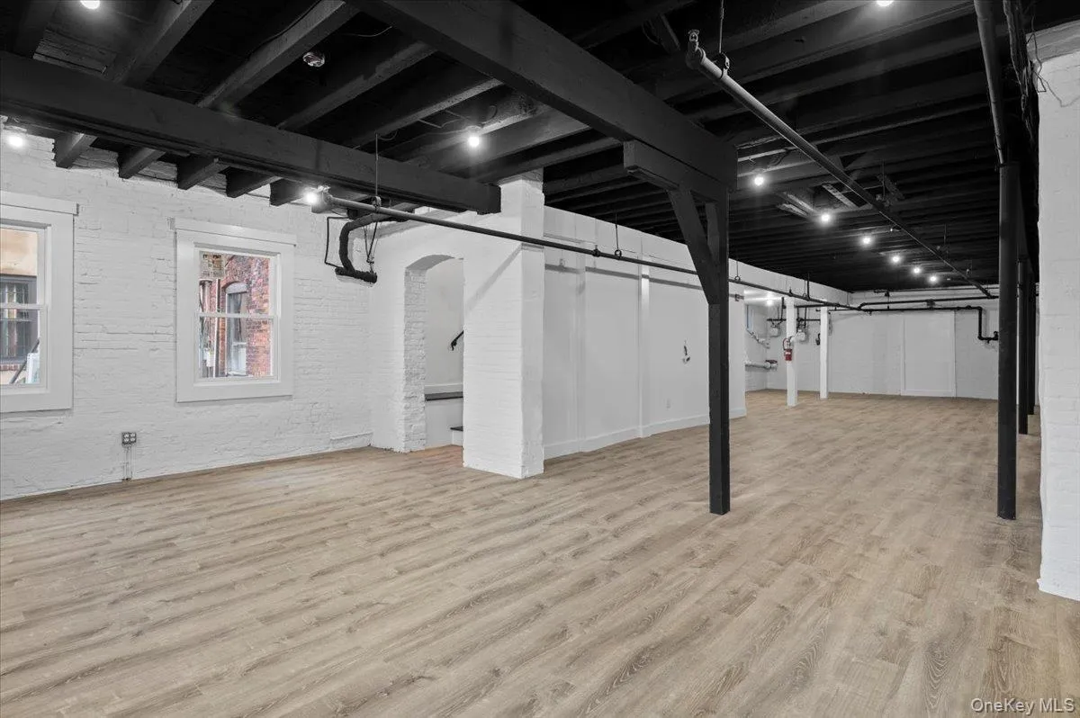 Below grade area with brick wall, light wood-style flooring, and arched walkways Below grade area with brick wall, light wood-style flooring, and arched walkways