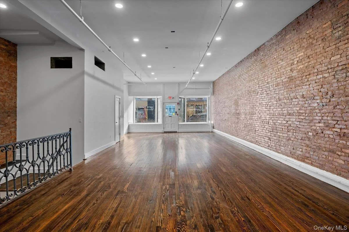 Unfurnished living room with brick wall, recessed lighting, dark wood finished floors, and a high ceiling Unfurnished living room with brick wall, recessed lighting, dark wood finished floors, and a high ceiling