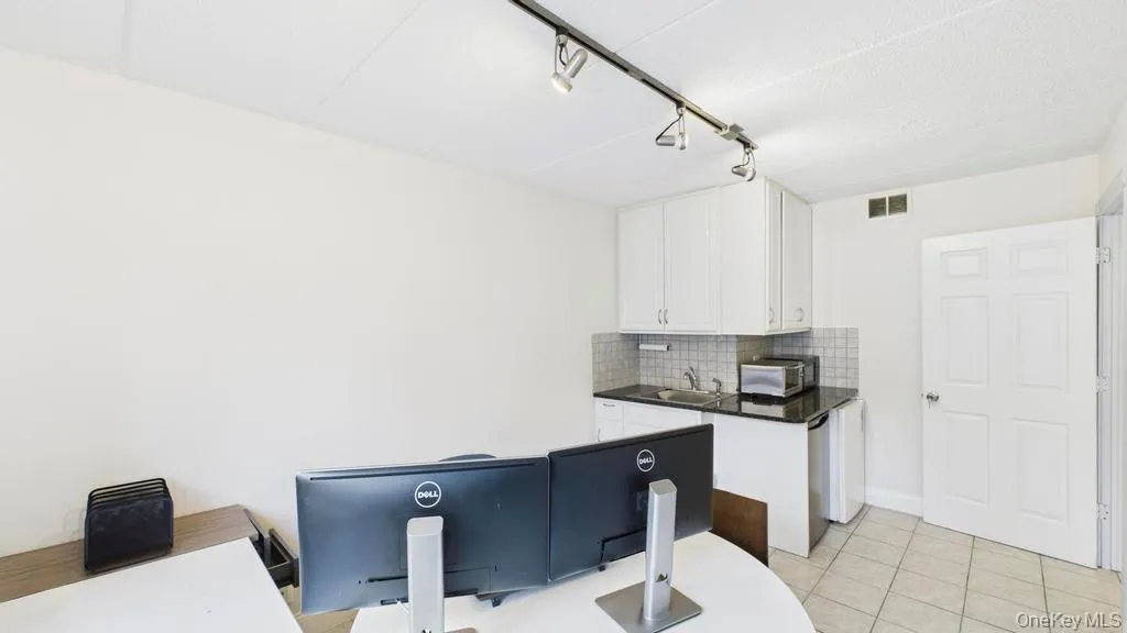 Kitchen with tasteful backsplash, white cabinetry, rail lighting, light tile patterned floors, and stainless steel microwave Kitchen with tasteful backsplash, white cabinetry, rail lighting, light tile patterned floors, and stainless steel microwave