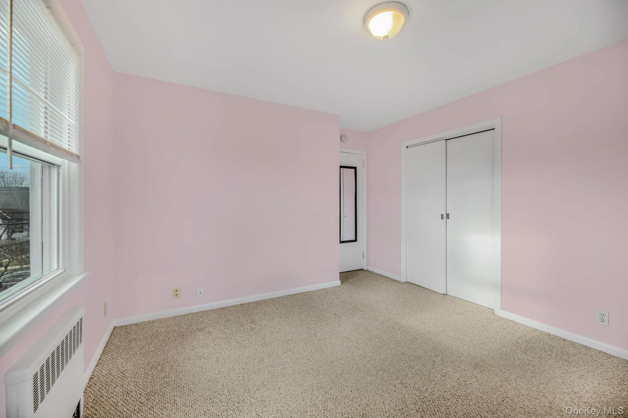 Unfurnished bedroom with radiator, carpet flooring, and a closet Unfurnished bedroom with radiator, carpet flooring, and a closet