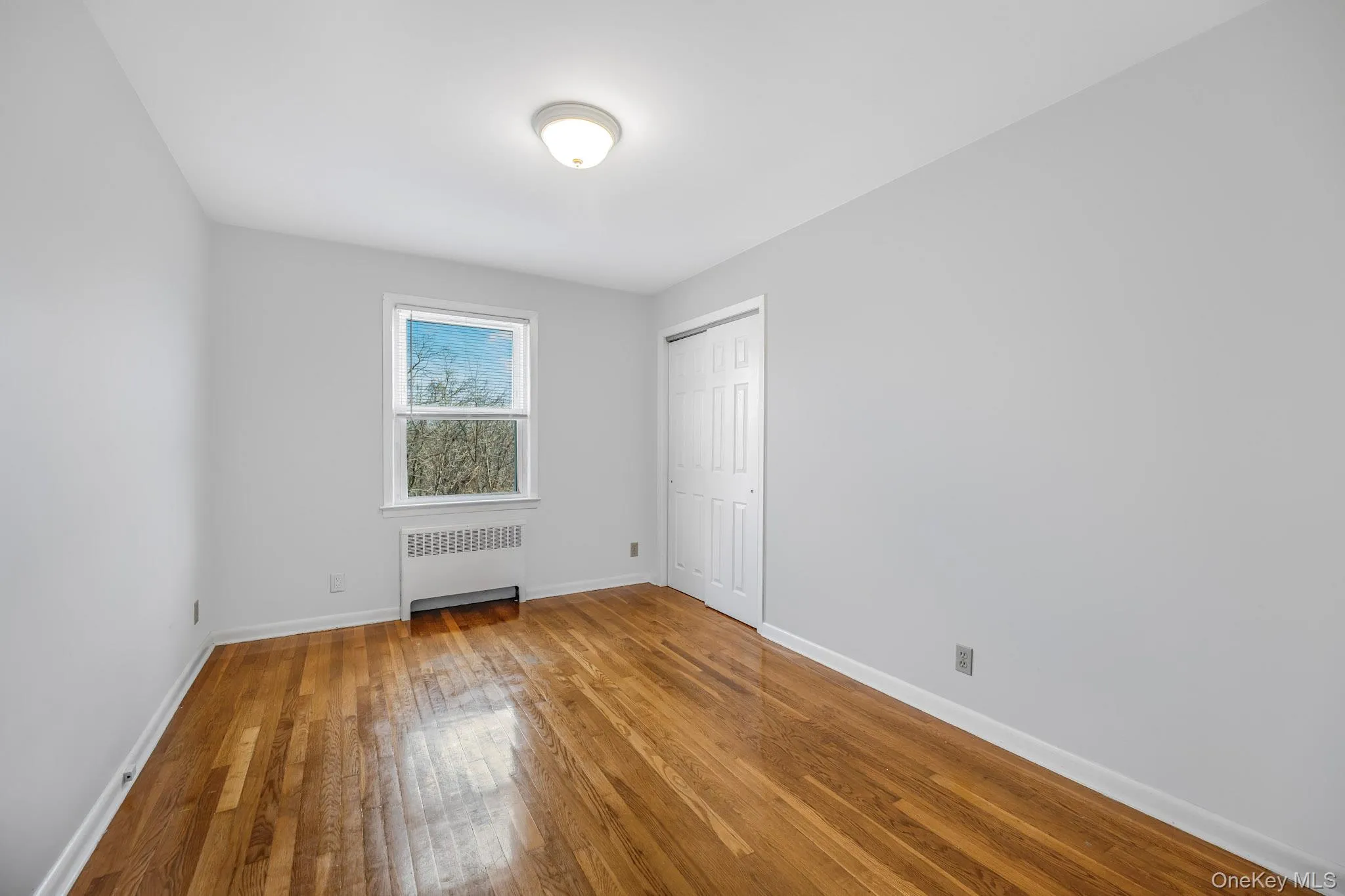 Unfurnished bedroom featuring radiator, light wood-type flooring, and a closet Unfurnished bedroom featuring radiator, light wood-type flooring, and a closet