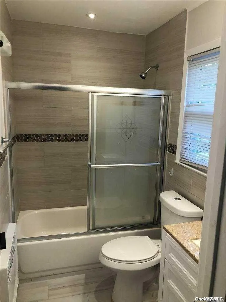 Full bathroom featuring vanity, toilet, tile walls, and combined bath / shower with glass door Full bathroom featuring vanity, toilet, tile walls, and combined bath / shower with glass door