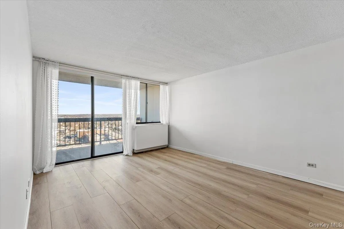 Empty room with a textured ceiling, light wood-style floors, and floor to ceiling windows Empty room with a textured ceiling, light wood-style floors, and floor to ceiling windows